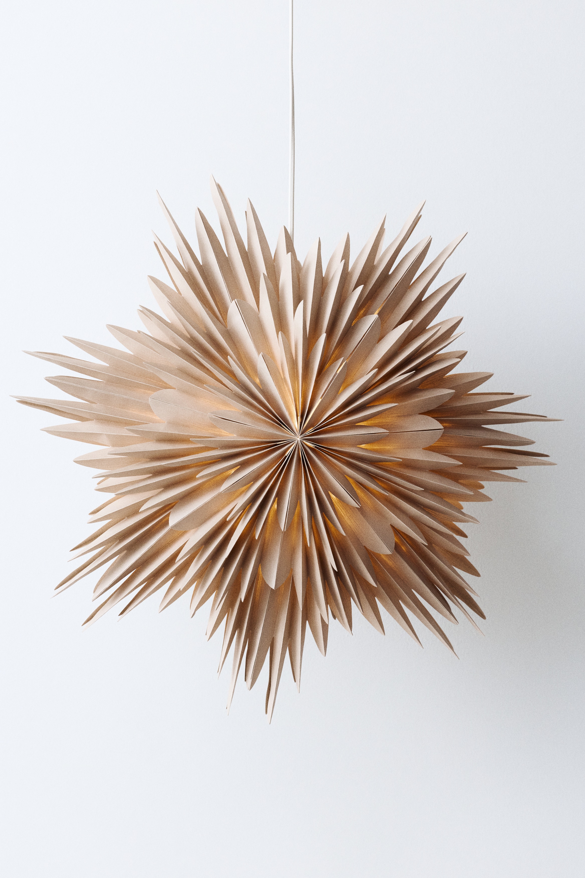 A light beige paper star decoration is facing forwards, displaying a multi-layered, three-dimensional design with numerous pointed, accordion-folded paper tips radiating outwards from a central point.