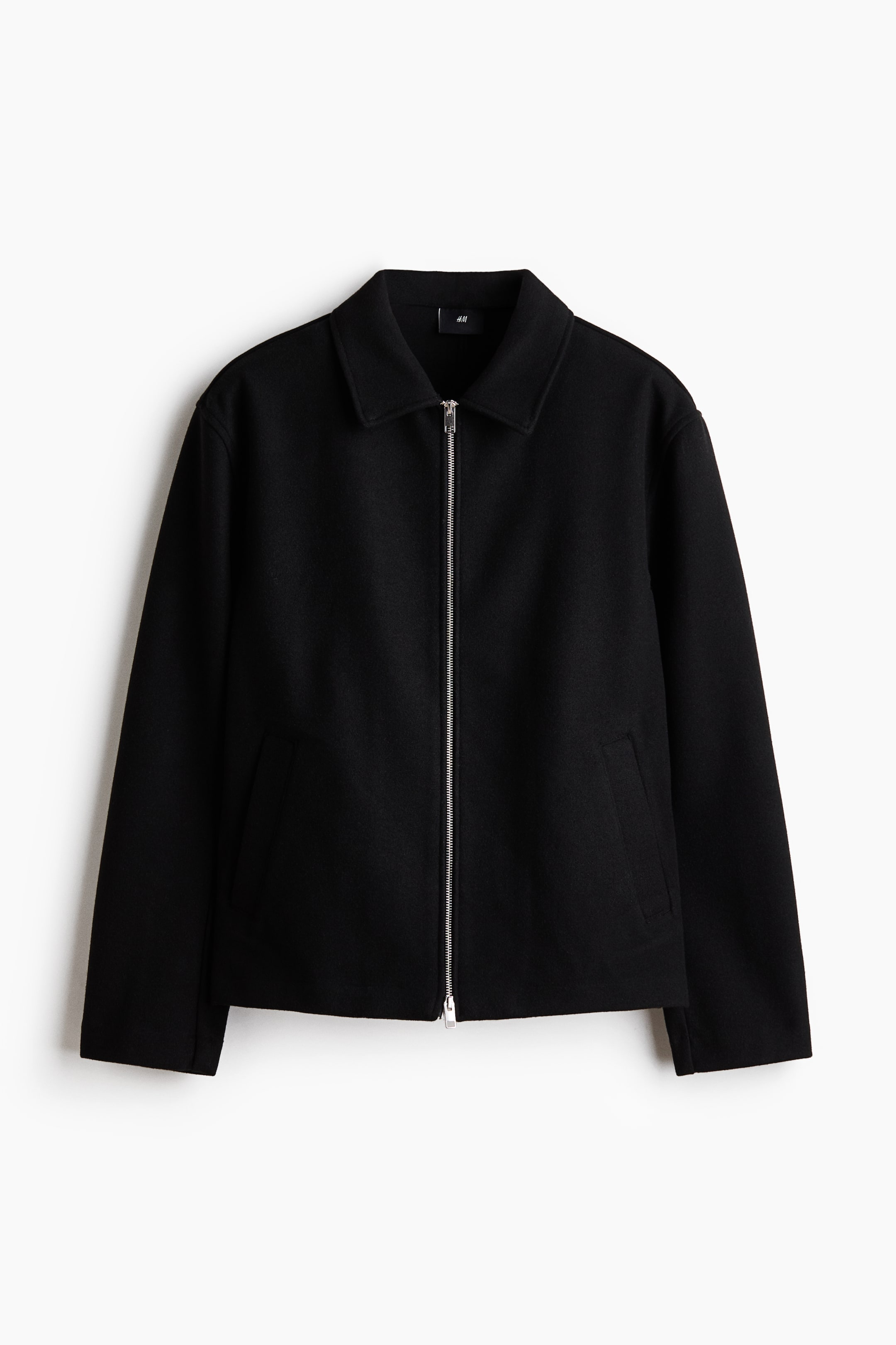 Größeres Bild ansehen: Eine schwarze Jacke ist von vorne präsentiert und verfügt über einen spitzen Kragen sowie einen durchgehenden silbernen Reißverschluss in der Mitte. Sie ist mit zwei schrägen Leistentaschen auf der Vorderseite, langen Ärmeln und einem geraden Saum gestaltet.