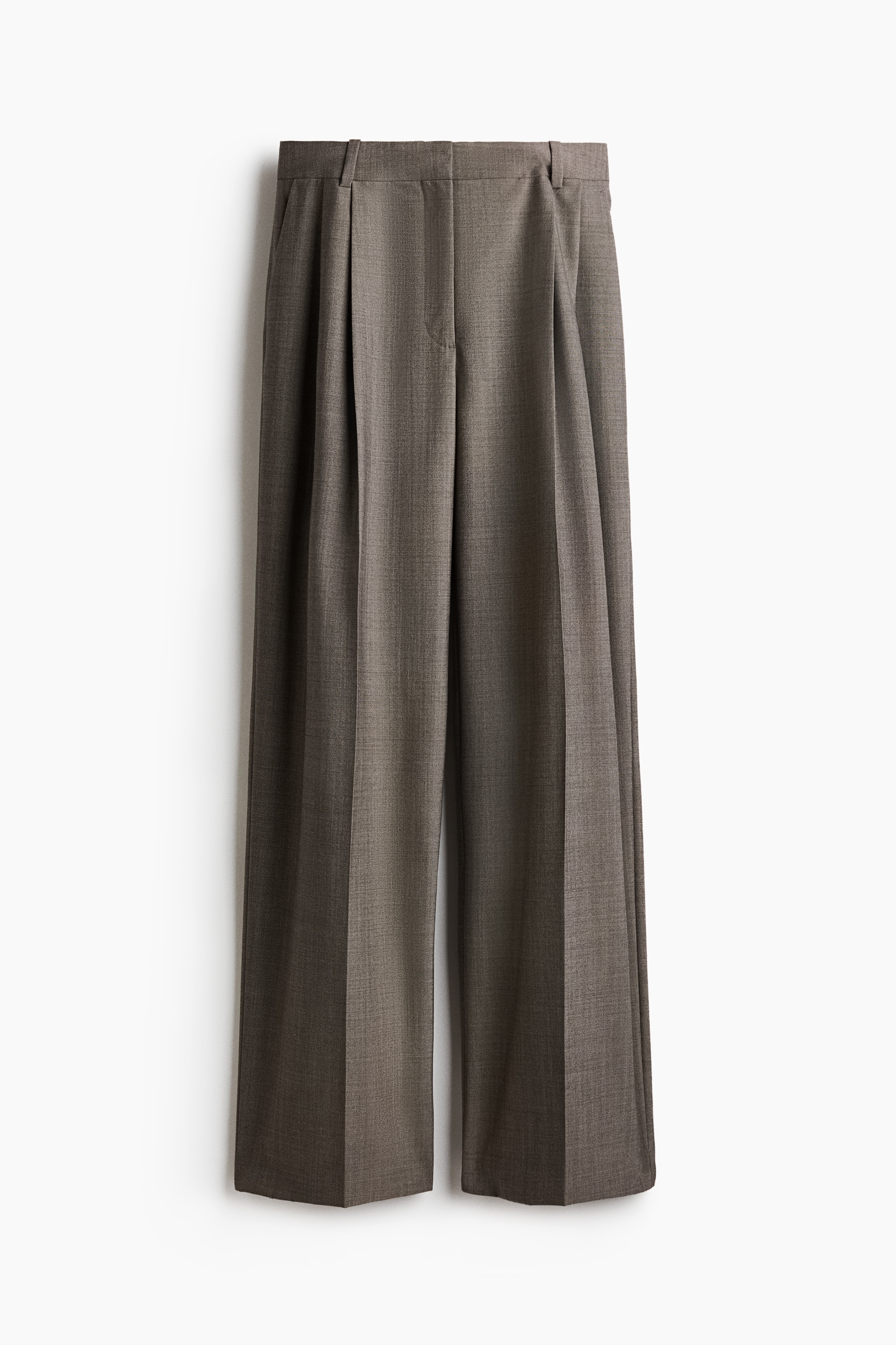 I pantaloni in tessuto misto lana grigio-marrone indossati dalla modella presentano una linea dritta e ampia, con pieghe sul davanti e pieghe nette. I pantaloni sono abbinati a un completo coordinato con blazer doppiopetto e scarpe bianche.
