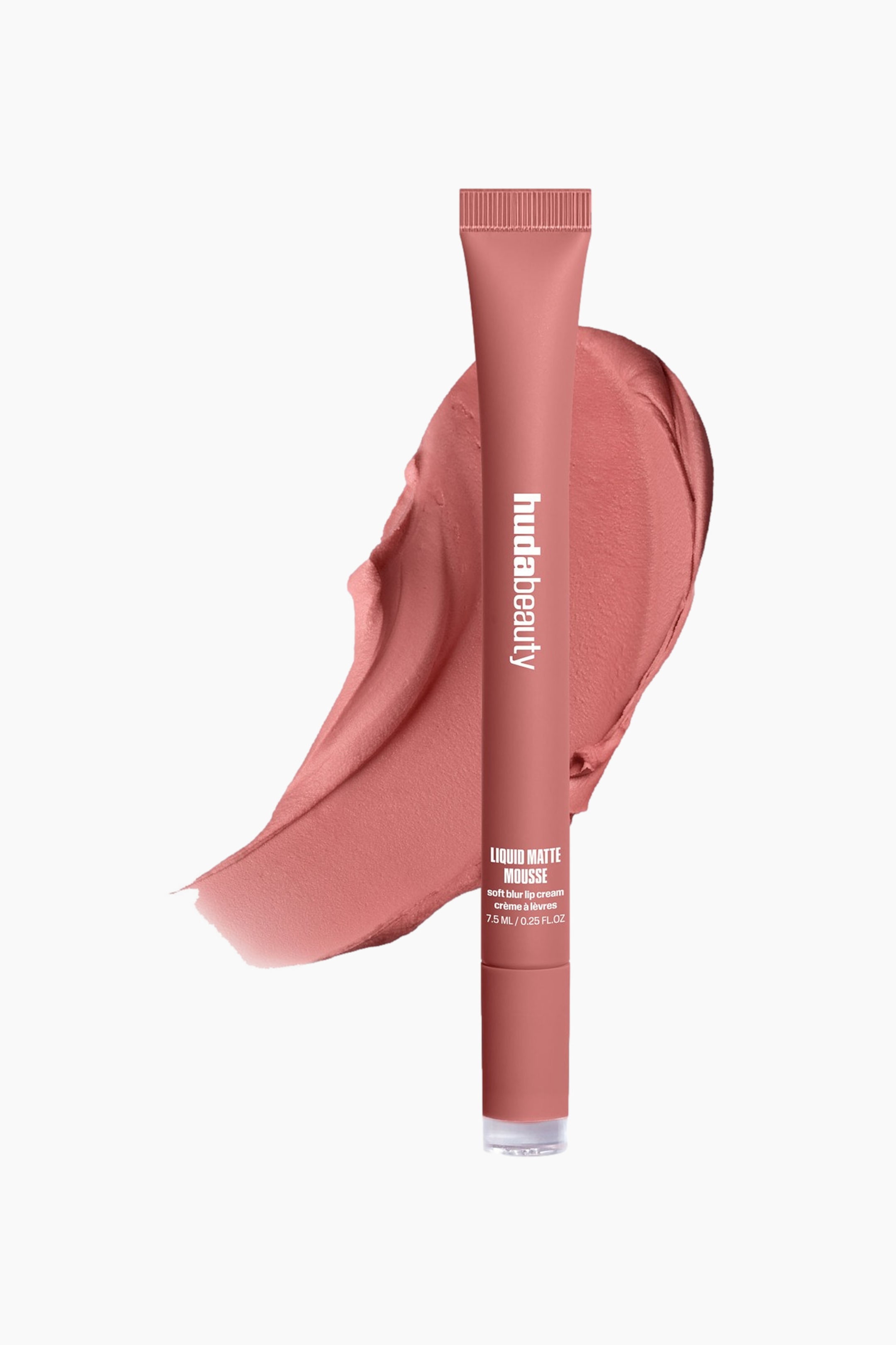 Visa större bild: En dämpad rödrosa Huda Beauty Liquid Matte Mousse-trycktub med räfflad topp, med vit brandingtext, står upprätt och lätt vinklad åt höger. Den är placerad framför ett virvlande streck av samma produktfärg, som sträcker sig åt vänster.