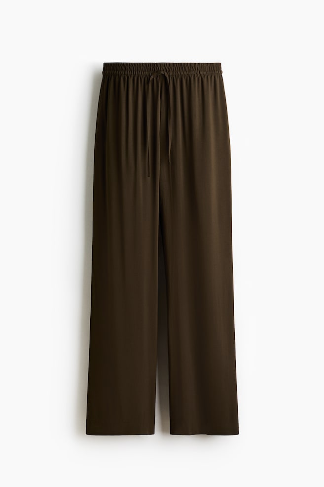 A pair of dark olive green wide-leg pants is featuring an elasticized waistband with a central drawstring tie, displayed from the FRONT. - 1