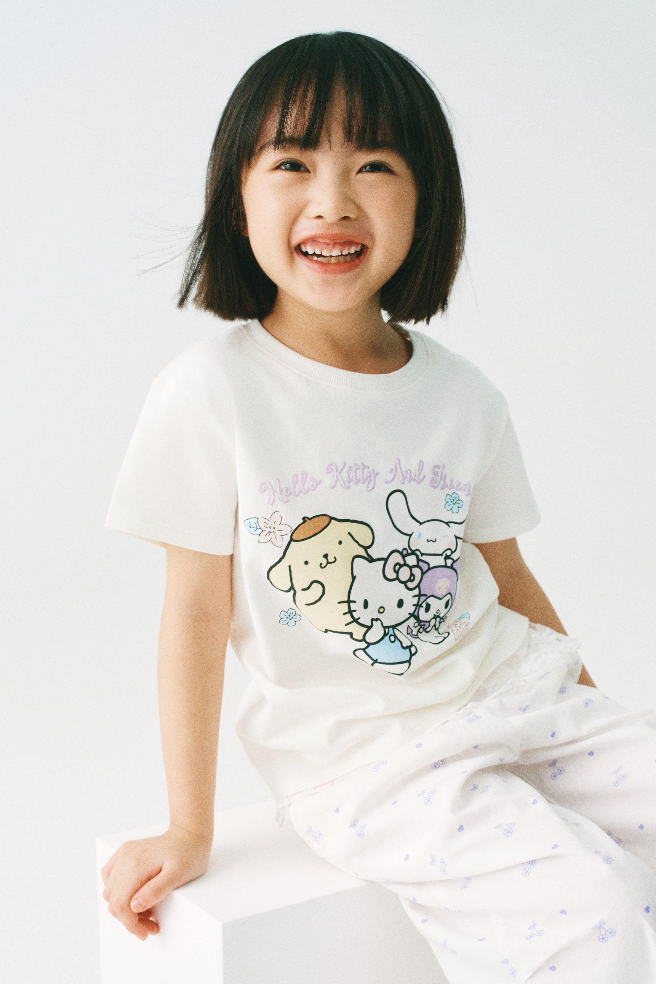 View larger image: The model is wearing a soft cotton jersey T-shirt with ribbed trim around the neckline. This white T-shirt showcases a vibrant graphic print on the front featuring "Hello Kitty And Friends."