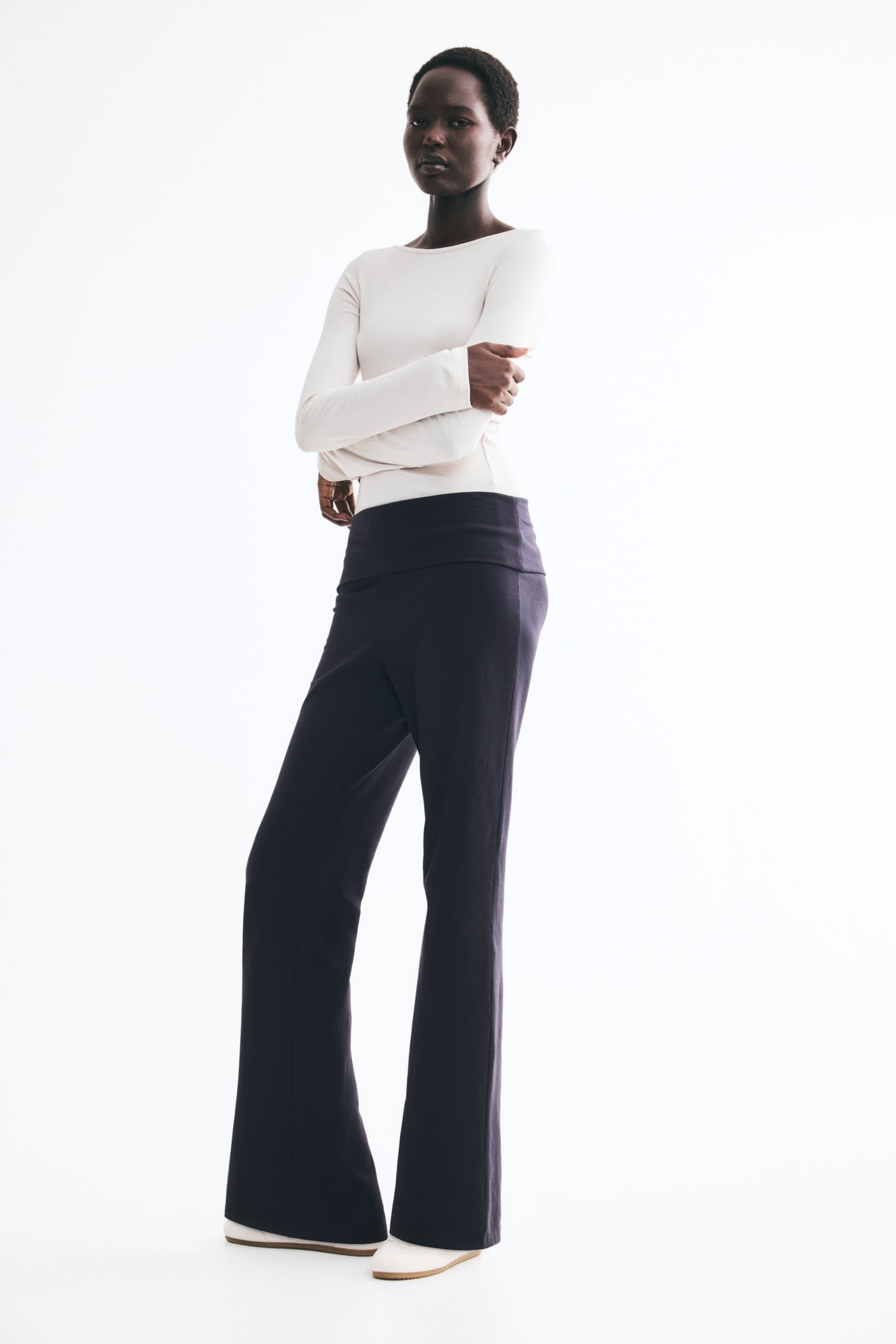View larger image: Dark cotton jersey pants featuring a wide, foldover waistband and straight legs that flare to the hems are being worn by the model. The pants are paired with a long-sleeved cream top.