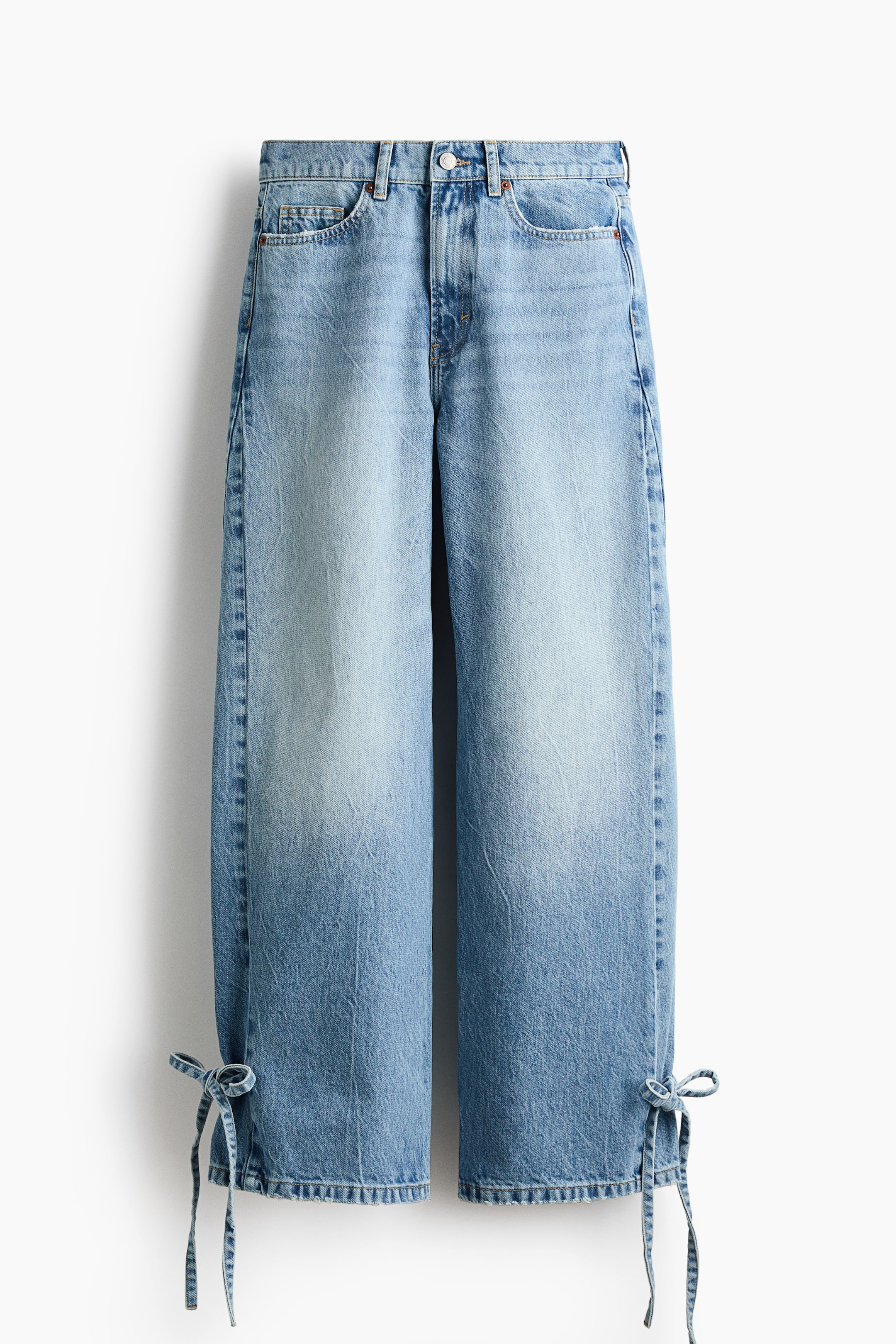 Büyük resmi görüntüle: Açık mavi denim kot pantolon çifti, ön görünümde sergileniyor ve geniş paçalara doğru koyulaşan soluk bir yıkama özelliği taşıyor. Her bacağın dış bileğinde denim bağcıklar fiyonklar oluşturuyor.