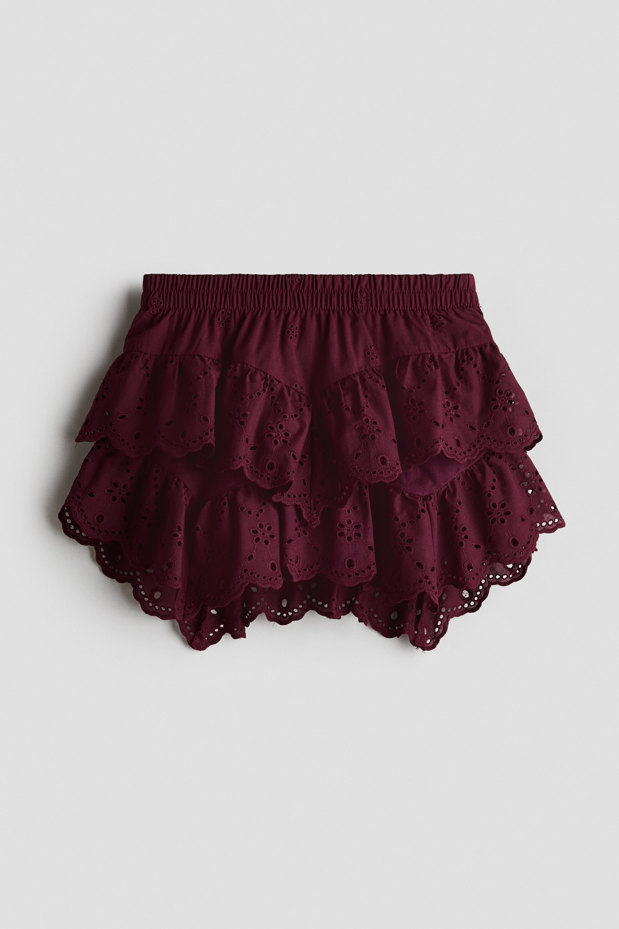 View larger image: A burgundy skirt featuring an elasticated waistband and two-tiered ruffles. The ruffles are detailed with eyelet embroidery and scalloped edges.