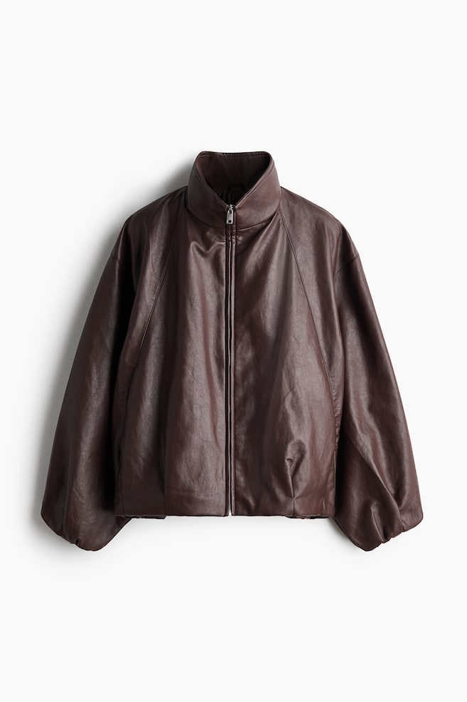 A dark brown leather-look jacket is facing forward and is featuring a high stand-up collar and a silver-toned zipper down the front. Its voluminous long sleeves are ending in gathered cuffs, and the cropped body is finishing with a slightly gathered hem. - 1