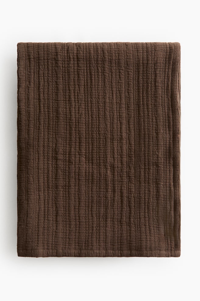 The single bedspread showcases a rich brown hue. It features a soft, crinkled cotton muslin weave with subtle vertical lines visible across its surface. - 1