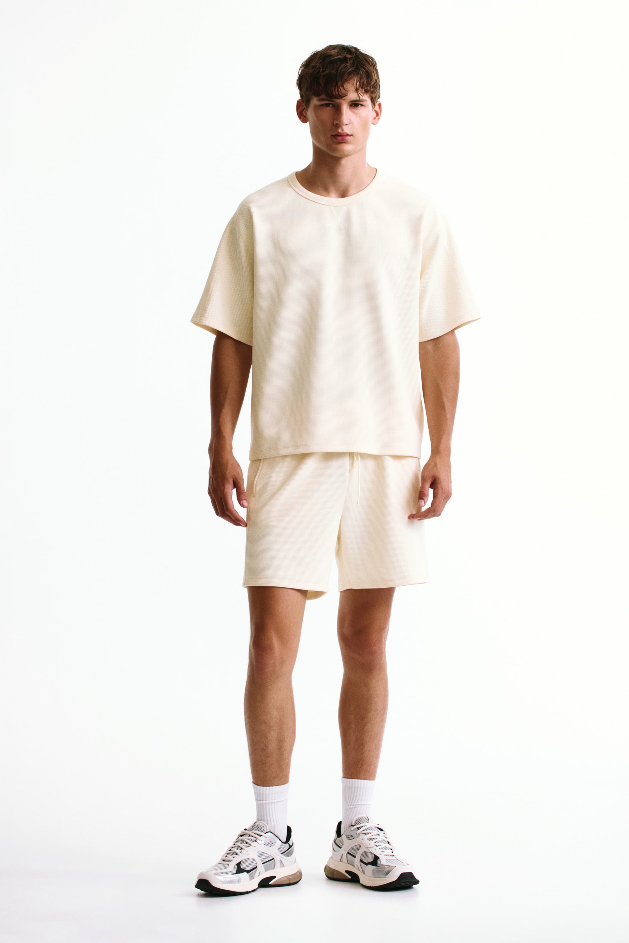 View larger image: The model is wearing Regular Fit Waffled sports shorts in a cream colour, featuring a subtle waffled texture, drawstring waist, and side pockets, styled with a matching cream T-shirt.