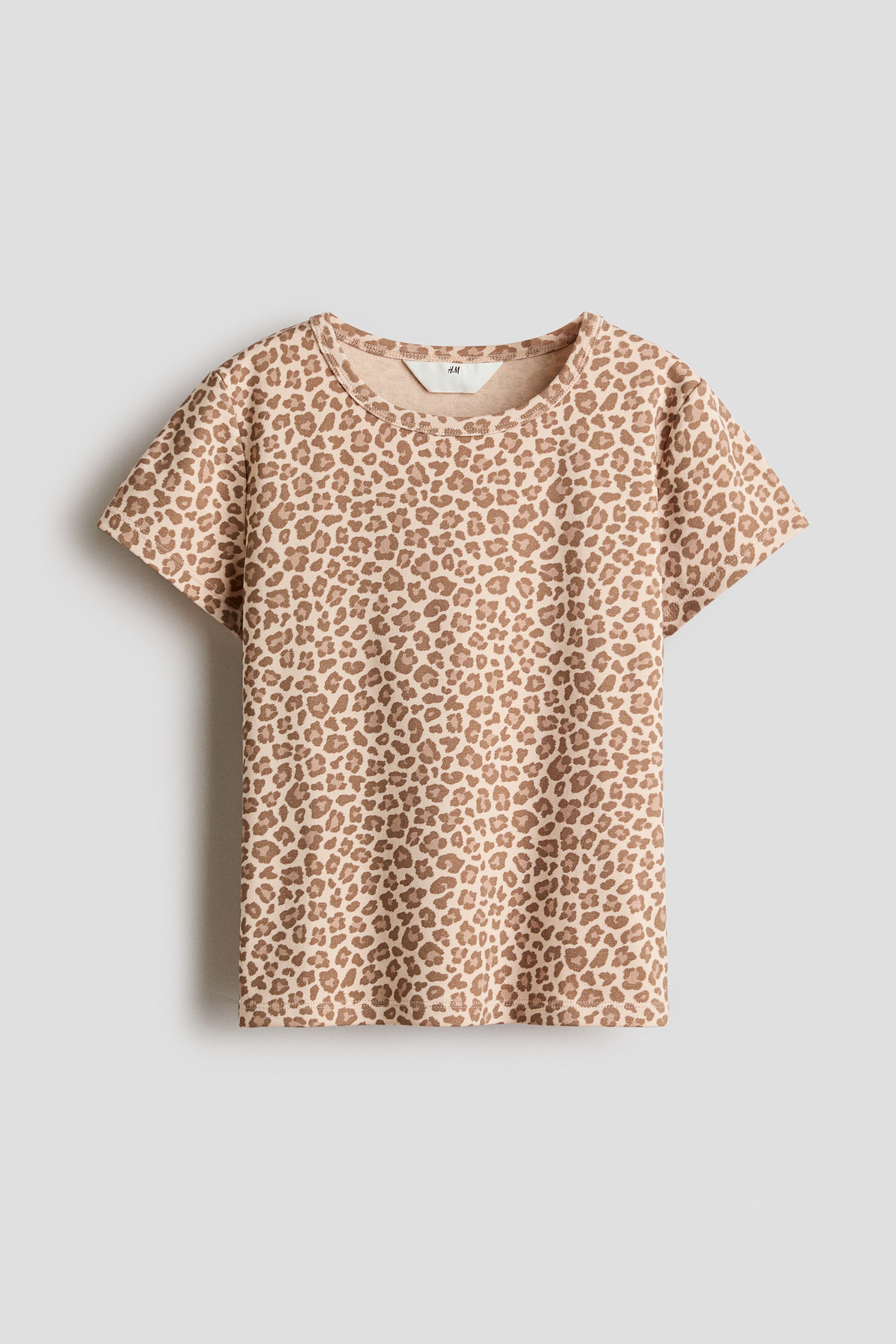 Agrandir l'image: Un t-shirt est présenté de face, affichant un imprimé léopard beige et marron sur un tissu en jersey. Il est doté de manches courtes et d'un col rond côtelé.