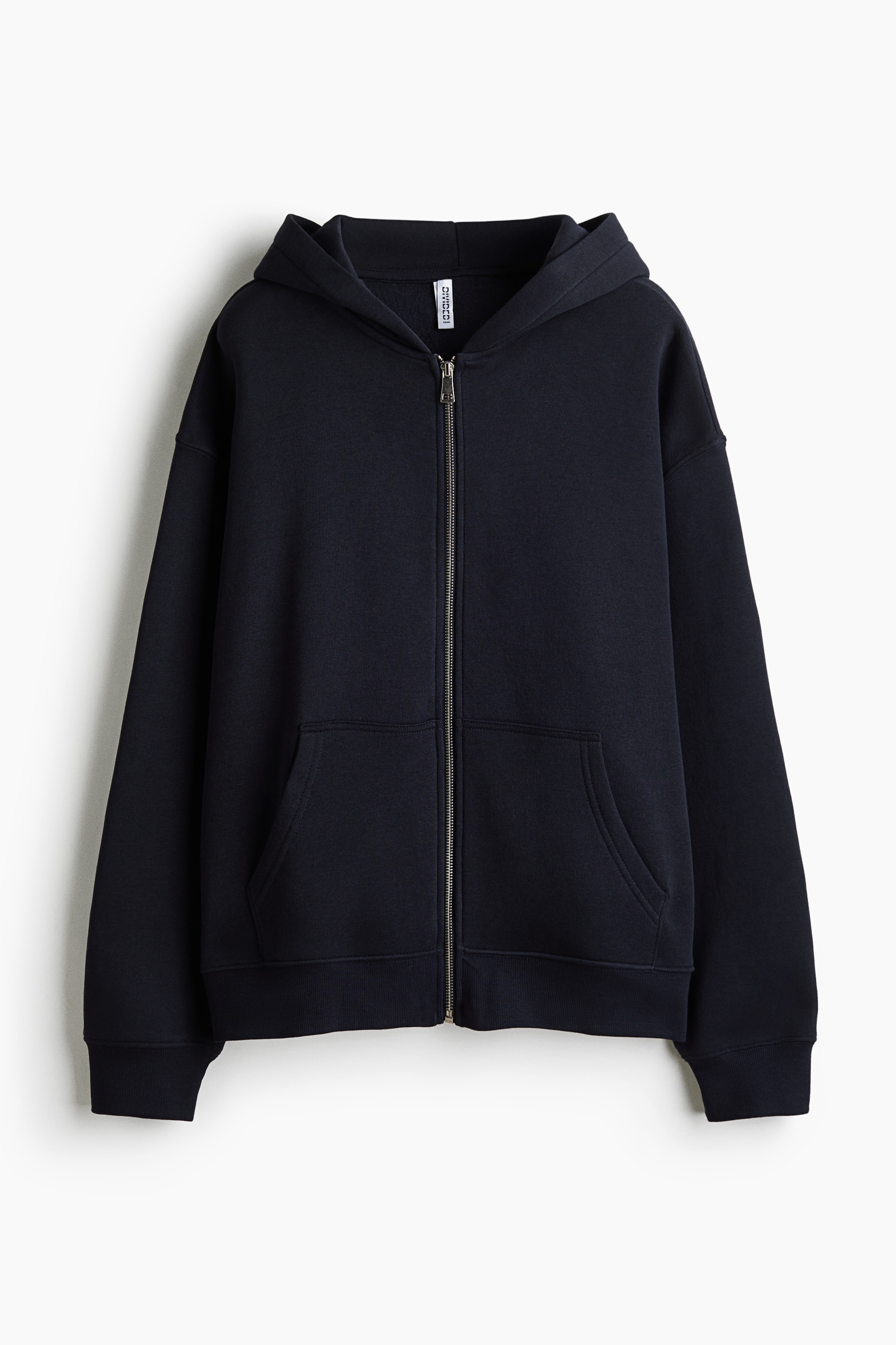 A black zip-up hoodie with "NEW YORK" printed in white arched text across the back is being worn by the model, who is facing away from the camera with the hood up. The model is adjusting the hood with both hands, styling the garment with light-wash, wide-leg denim jeans.