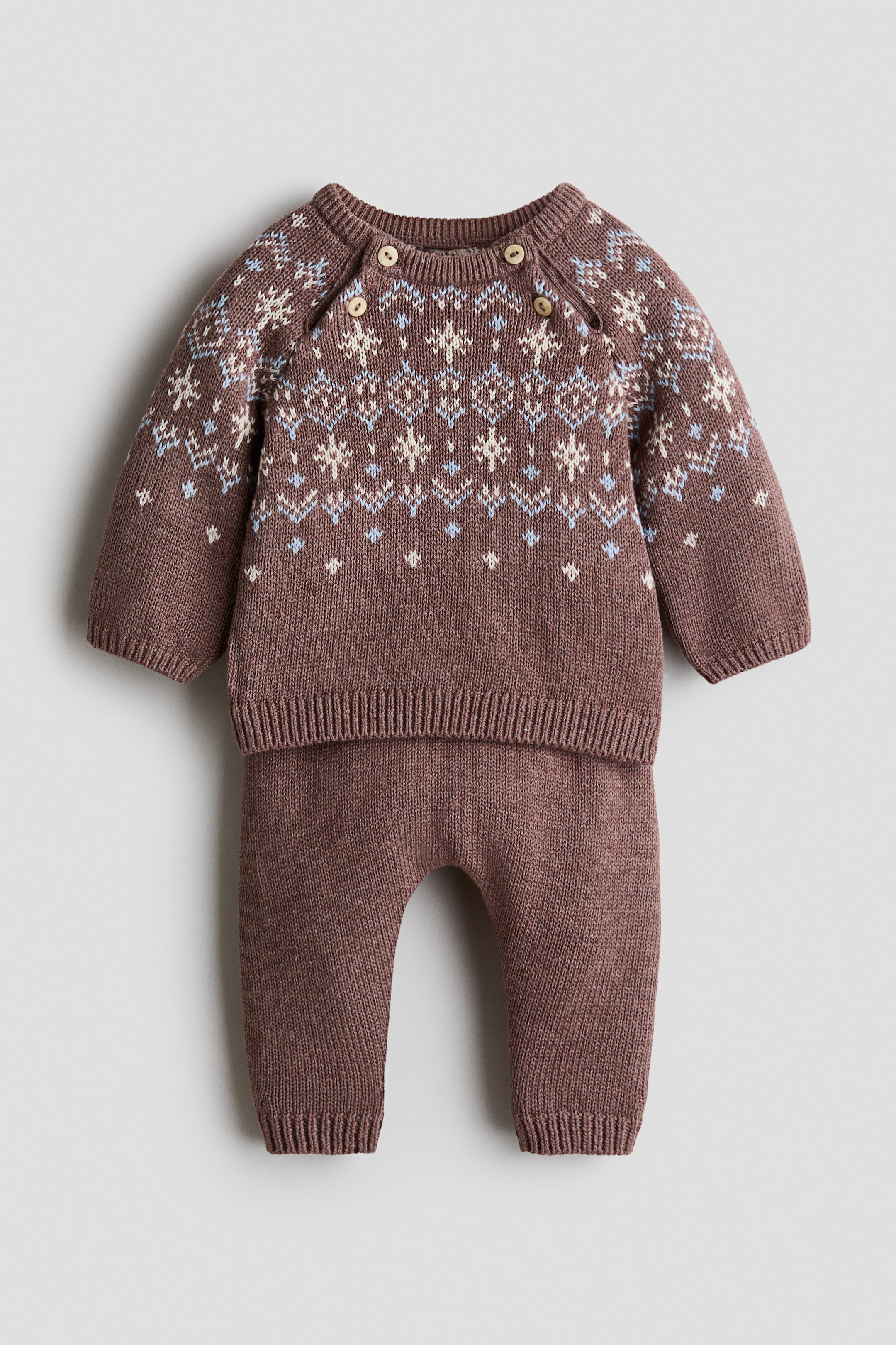 Ampliar la imagen: Un conjunto de punto para bebé en rosa polvo presenta un suéter con un patrón fair isle en crema y azul claro en el pecho y los hombros, tres botones de madera en el hombro izquierdo, puños acanalados y dobladillo acanalado. Un pantalón a juego completa el conjunto con puños acanalados en los tobillos.