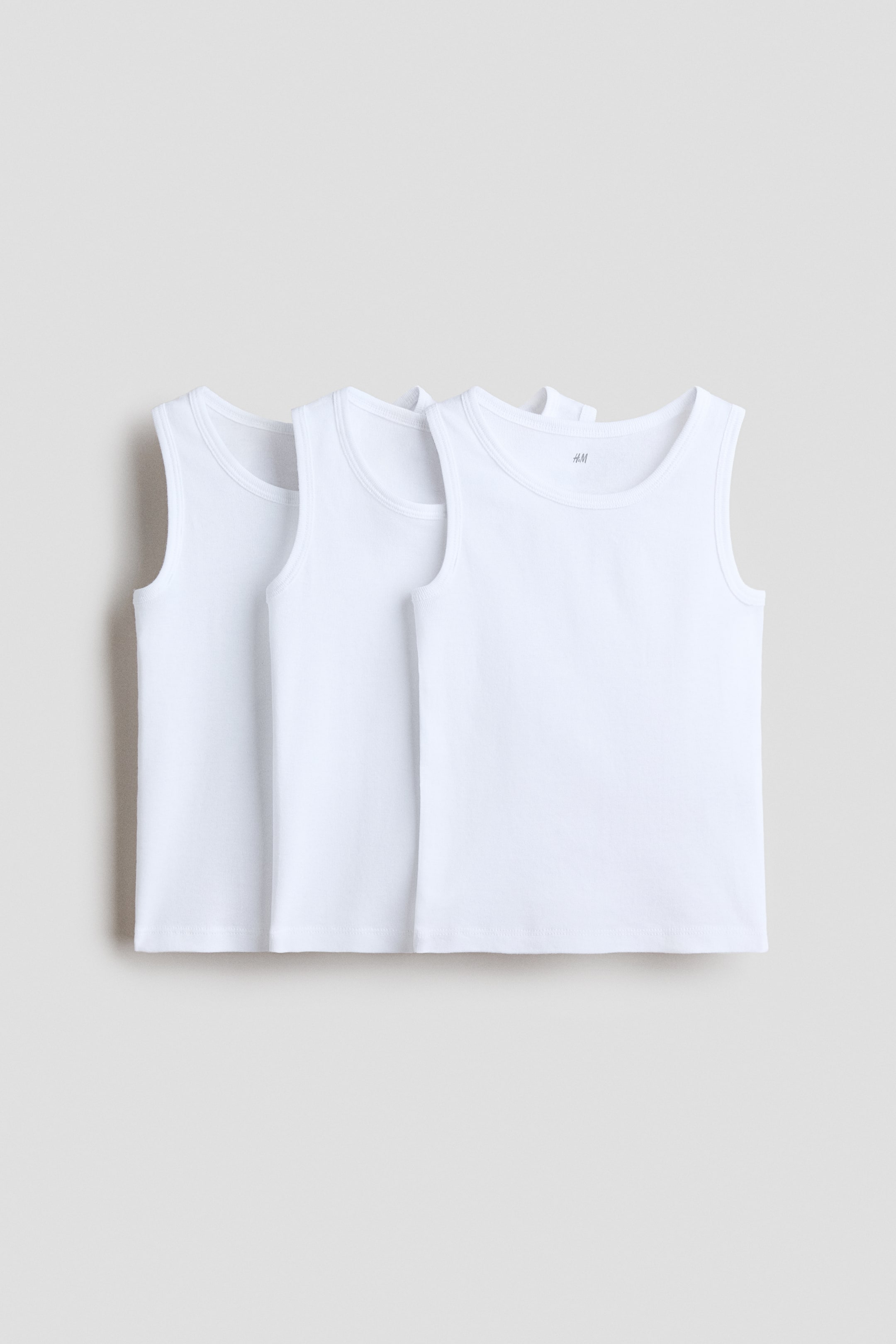 View larger image: Three white tank tops are displayed in layers, facing forward. Each top showcases a smooth knit fabric, a round neckline, wide shoulder straps, and a discreet brand label located at the inner back neck.
