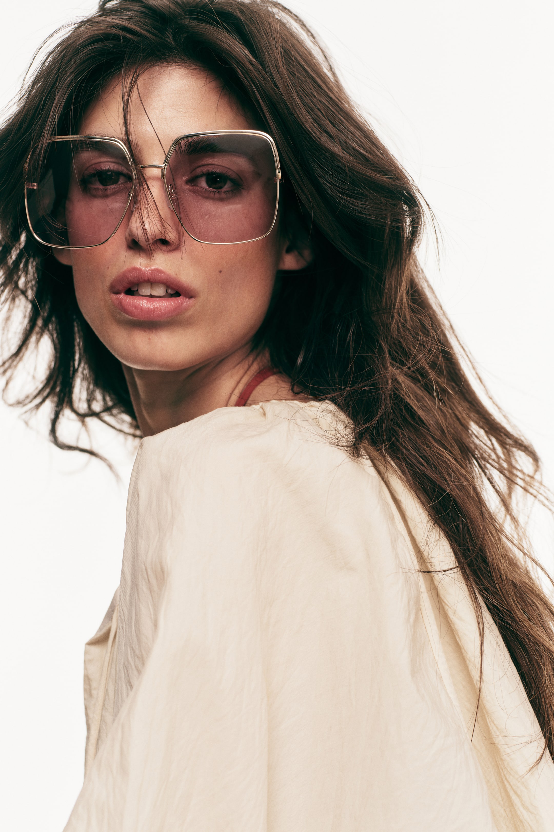 View larger image: Oversized square sunglasses feature thin gold-toned metal frames and pink-tinted lenses. They are positioned on a person's face, angled slightly to the right.