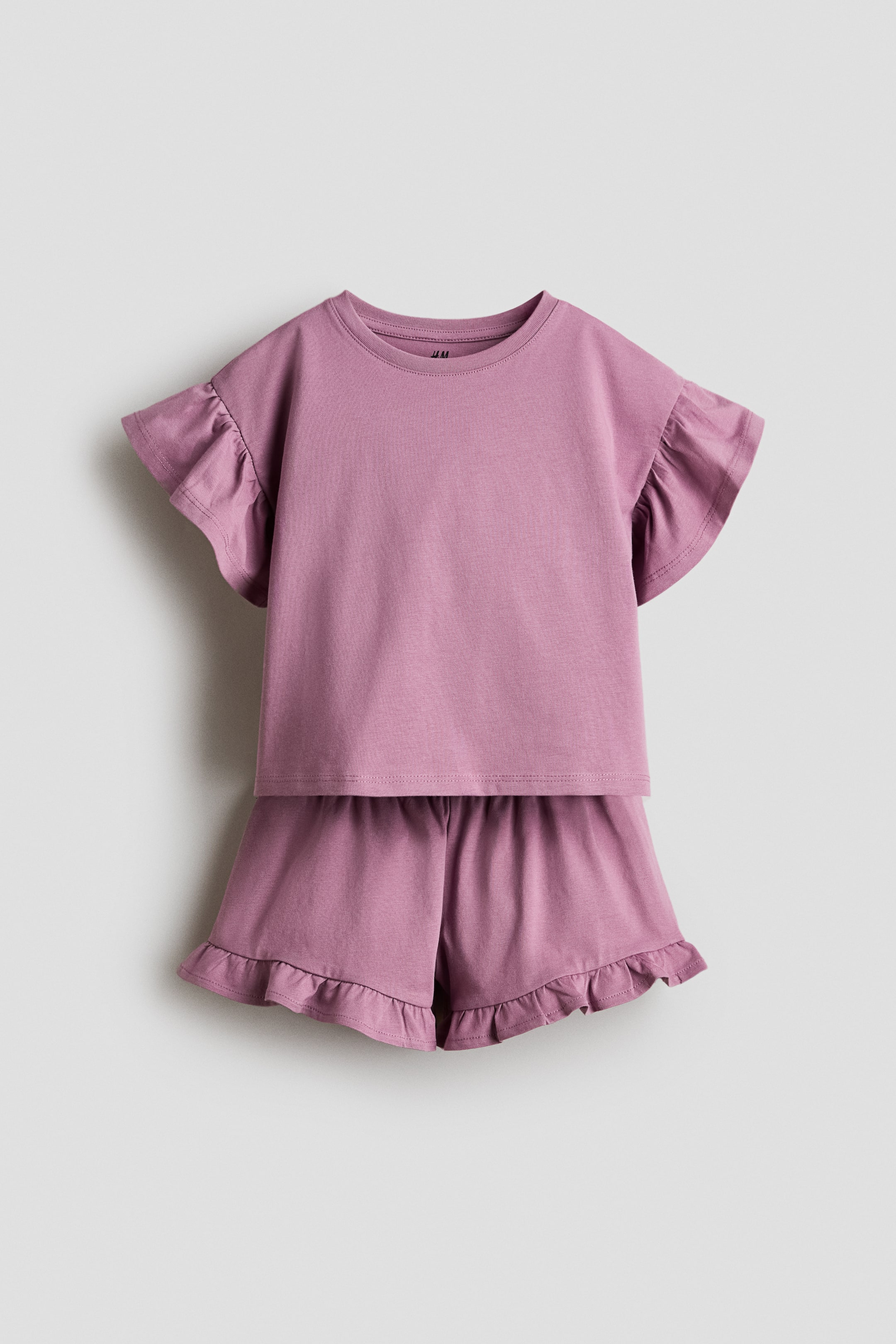 View larger image: A soft purple set crafted from cozy cotton jersey is showcased from the front, highlighting a top with a round neckline, dropped shoulders, and flutter sleeves, paired with shorts featuring an elastic waistband and frill-trimmed hems.