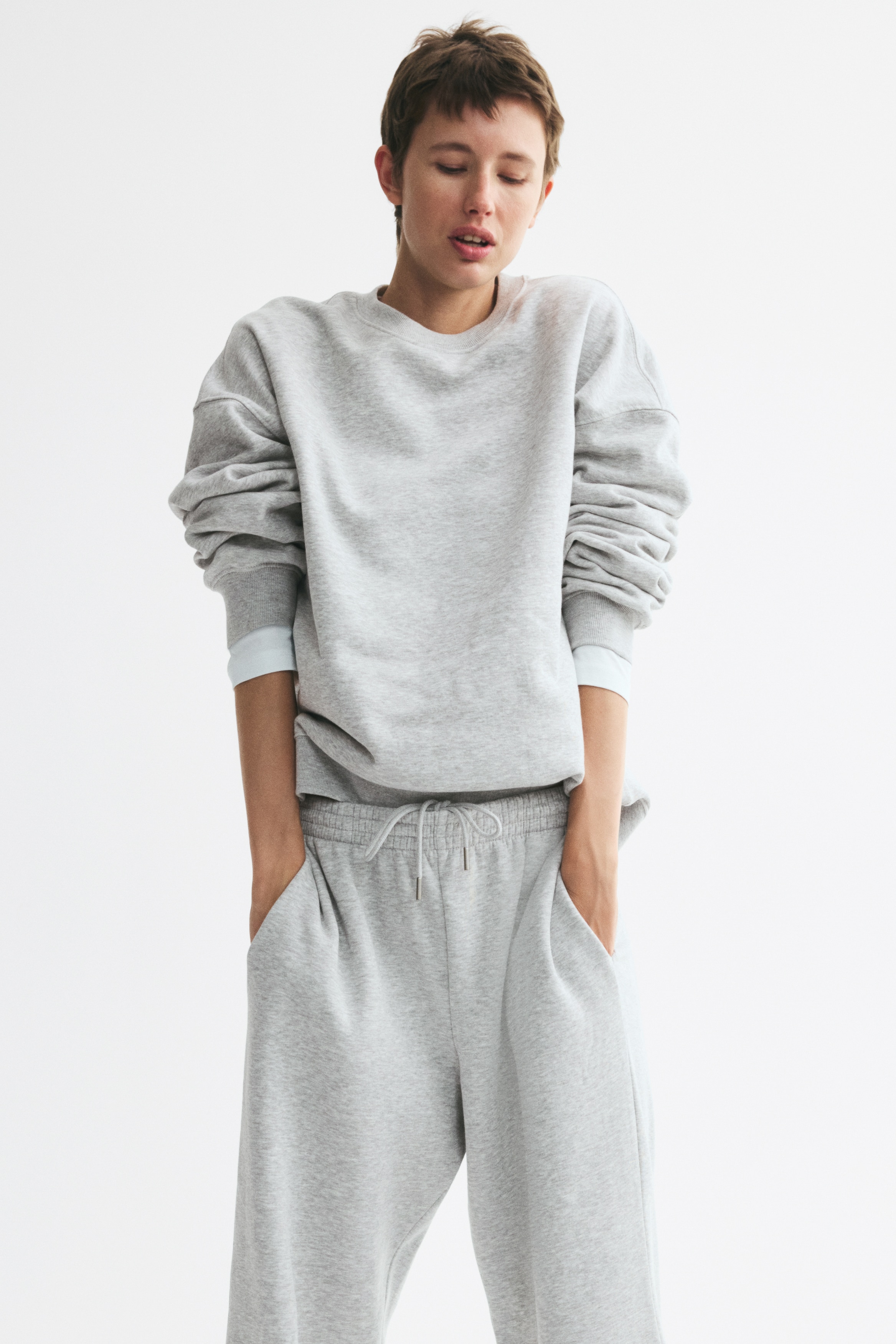 Lichtgrijze joggingbroek toont een vooraanzicht, met een elastische gesmokte tailleband, zijzakken en rechte pijpen in een gemêleerde sweatshirtstof.