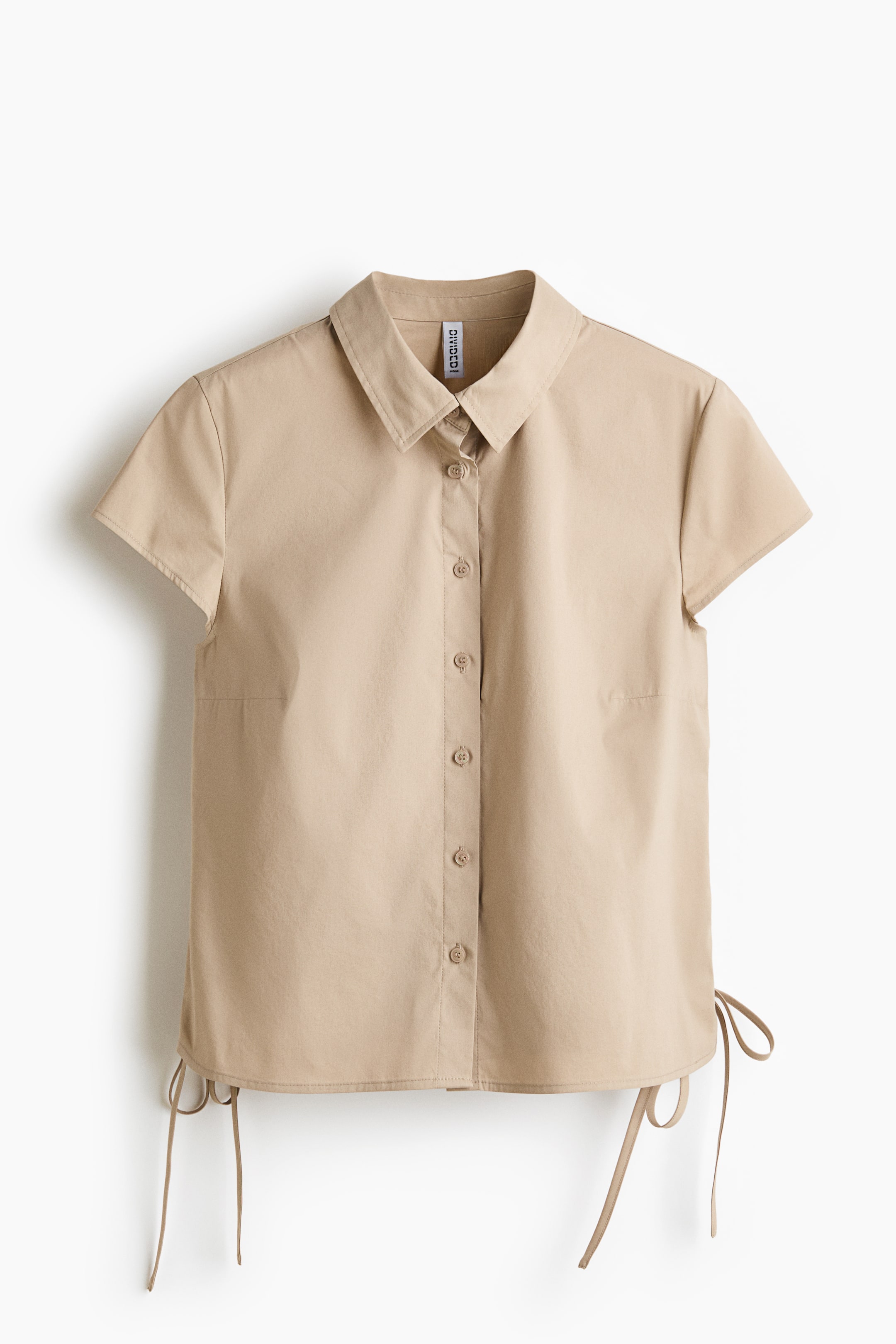 View larger image: A beige short-sleeved shirt is showcasing its front, with a pointed collar and a full button-front placket adorned with matching buttons. Crafted with cap sleeves, it includes adjustable drawstrings on both sides of the bottom hem, elegantly tied into bows.