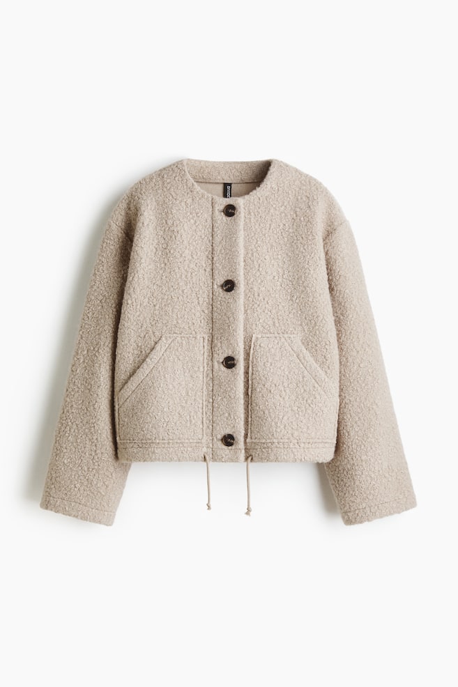 A light beige bouclé jacket is presenting FRONT, featuring a collarless round neckline and a button-front closure with four dark brown buttons. Two angled patch pockets are visible on the front, and an adjustable drawstring is detailing the hem. - 1