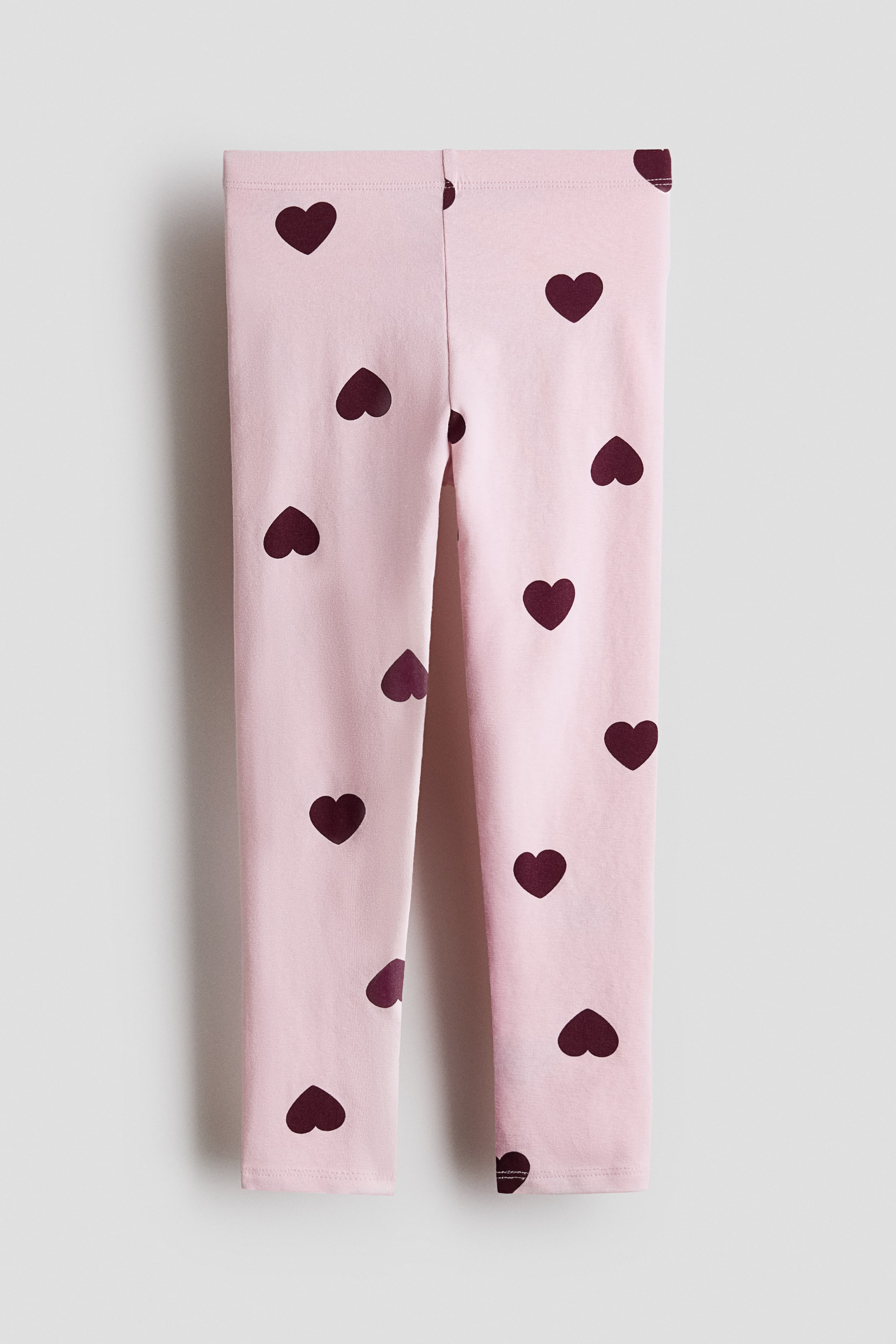 View larger image: Leggings in soft cotton jersey are shown from the front in a light pink shade with scattered dark-red heart prints. They feature an elasticated waistband.