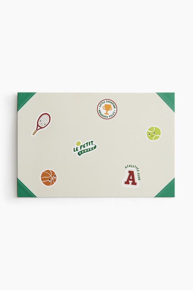 En rektangulÃ¤r skrivbordsunderlÃ¤gg i benvitt, sedd framifrÃ¥n, visar olika sportsillustrationer i tecknad stil utspridda Ã¶ver ytan, inklusive en basketboll, ett tennisracket, en tennisboll, en trofÃ© och ett varsity-bokstav "A". UnderlÃ¤gget har grÃ¶na triangelformade hÃ¶rnskydd med vit sÃ¶mnad i varje hÃ¶rn. - 1