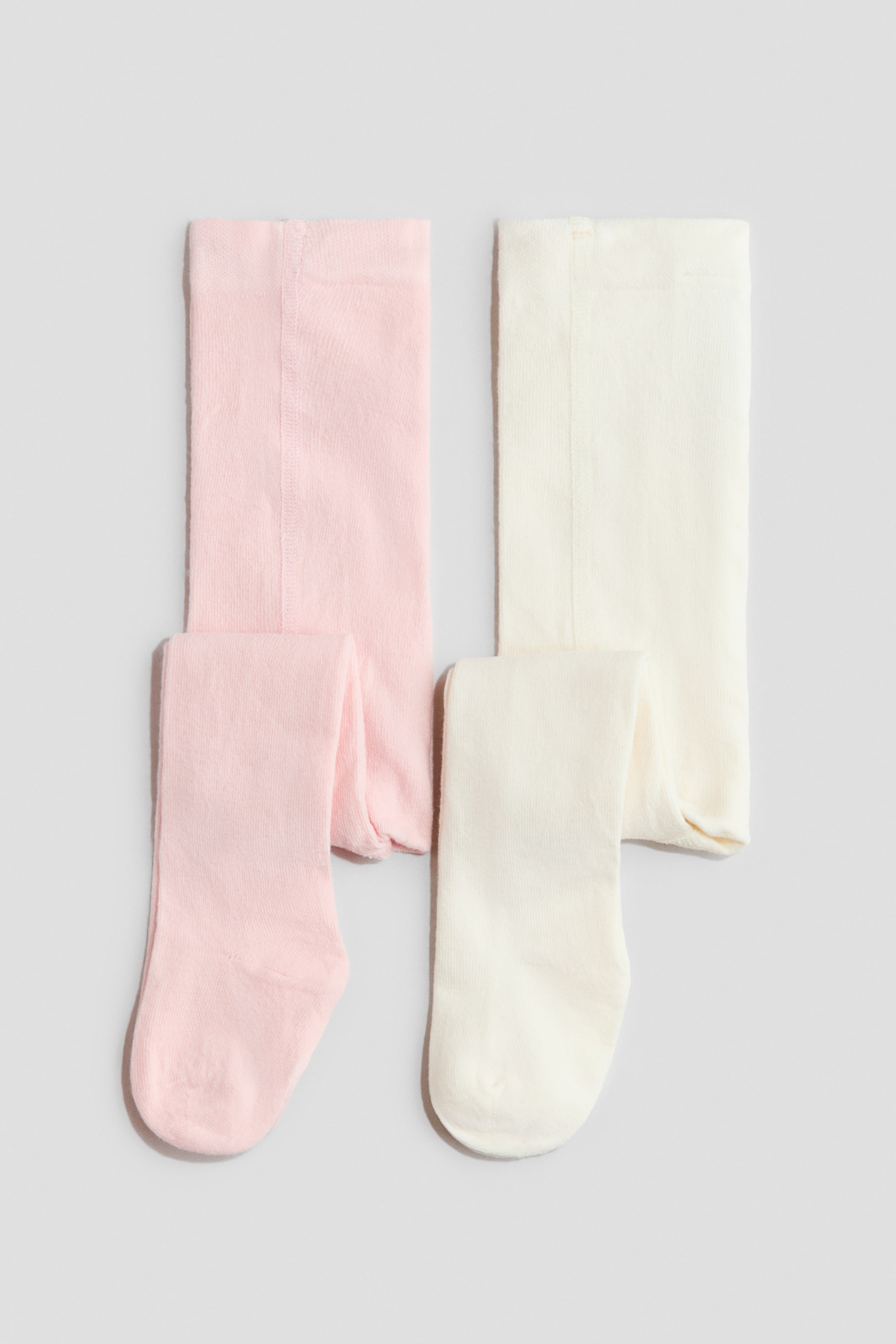 View larger image: Two pairs of baby tights are laid out flat, showcased in light pink and off-white shades. Each pair is neatly folded, highlighting its soft knit texture along with visible foot and lower leg sections.