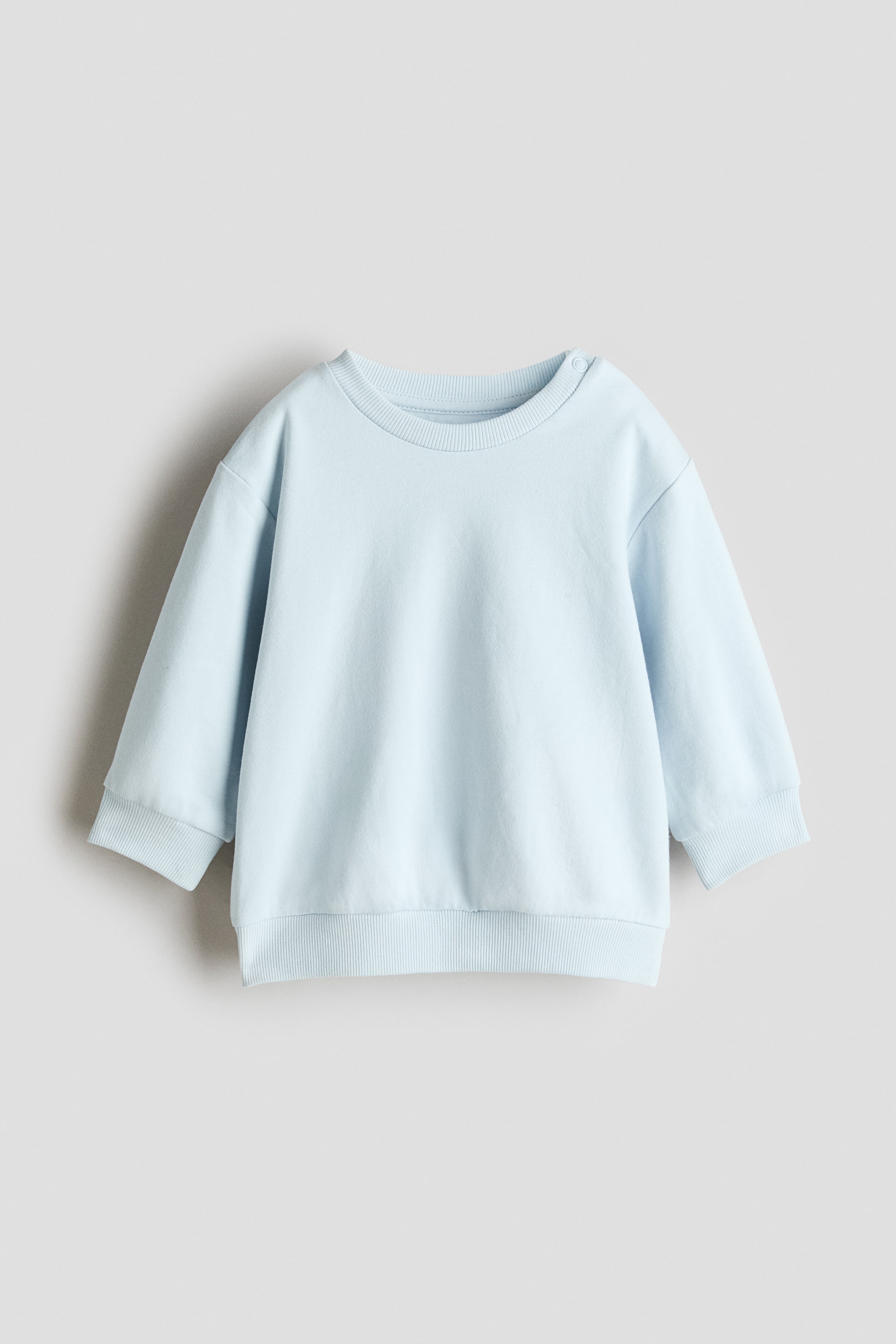 View larger image: A light-blue, long-sleeved sweatshirt is shown from the front. It features a ribbed crew neckline with a visible press-stud closure on the left shoulder, and is finished with ribbed cuffs and a ribbed hem.