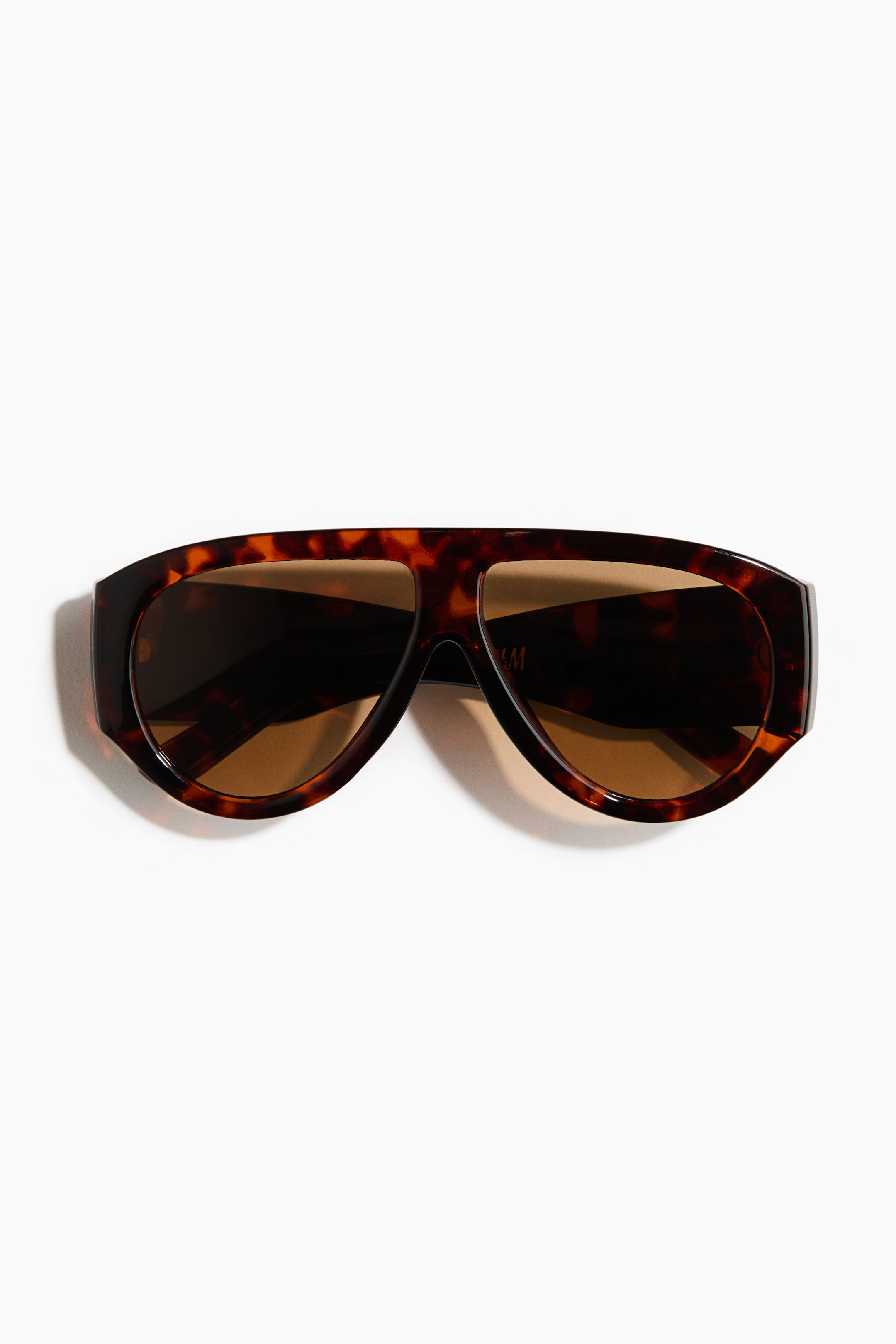 View larger image: A pair of sunglasses featuring a wide, front-facing, shield-style tortoiseshell frame with thick temples and brown tinted lenses.