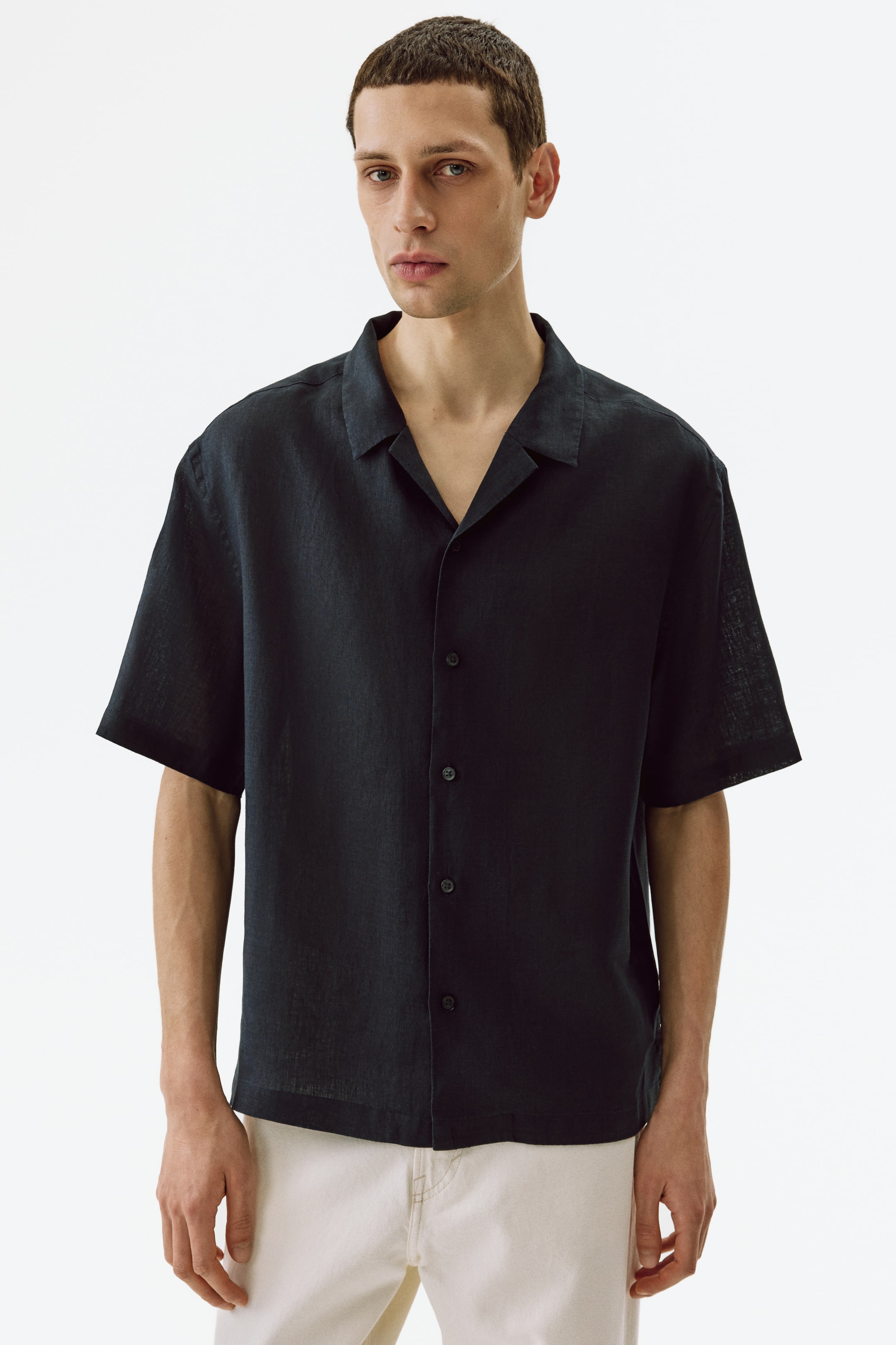 View larger image: Model tersebut memakai baju linen hitam berlengan pendek dengan kolar resort dan bahagian depan gaya Perancis. Baju ini menampilkan potongan santai dan hem lurus, serta dipadankan dengan seluar berwarna terang.