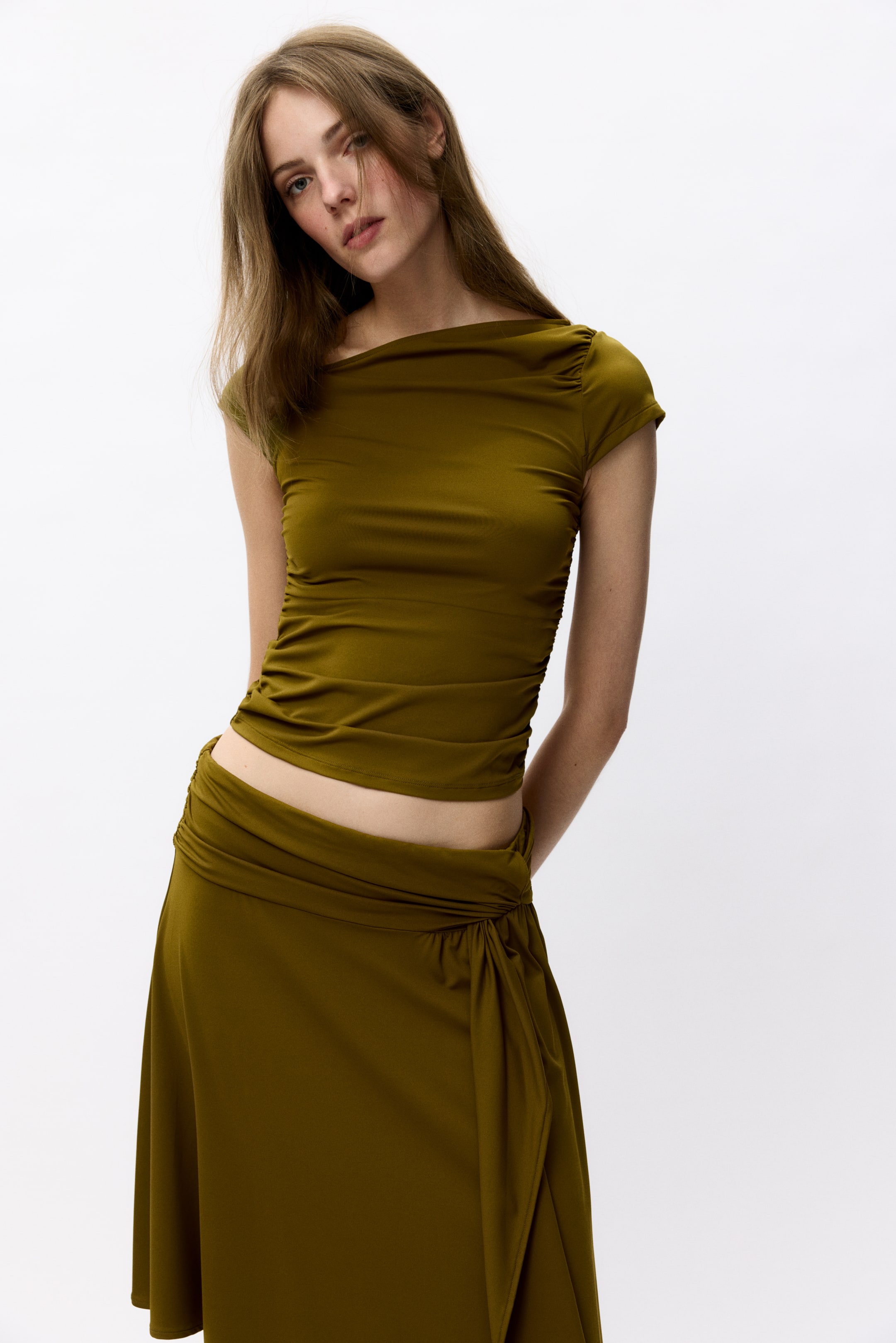 View larger image: The olive green cropped top features an asymmetrical draped neckline and short ruched sleeves. The matching midi skirt showcases a draped waist with a knot detail and a side slit, with both pieces fitting closely and draping fluidly.