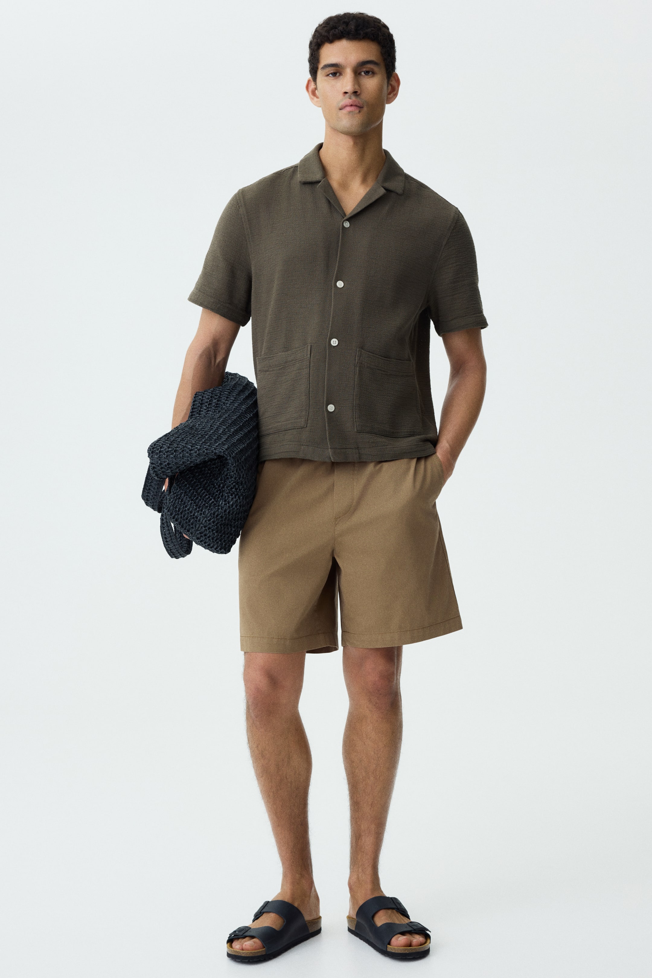 View larger image: An olive green short-sleeved shirt, displayed facing forward with a relaxed fit, features a textured fabric, a camp collar, a full button-front with light buttons, and two patch pockets on the lower front.