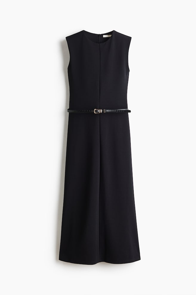 A front-facing view of a long, sleeveless black dress in structured ponte fabric, featuring a round neckline and a prominent vertical seam running down the center. A thin black belt with a gold-tone metal buckle is cinching the waist, with the slim-fit silhouette flaring gently toward the hem. - 1