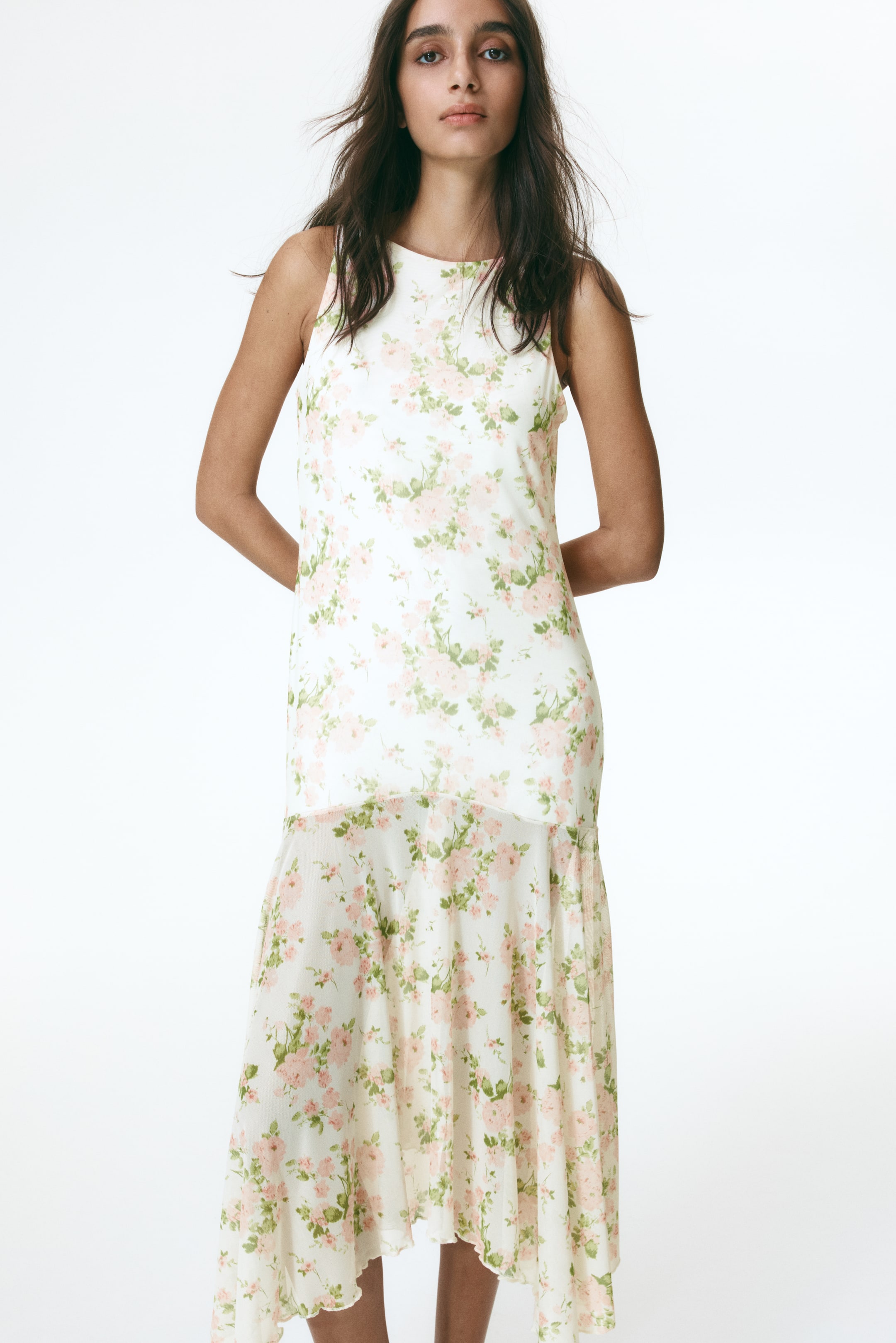 View larger image: A white sleeveless dress adorned with a light pink floral pattern is showcased facing forward. It boasts a round neckline and a tiered design, featuring a shorter top layer reaching mid-thigh and a longer bottom layer with an asymmetrical hemline.