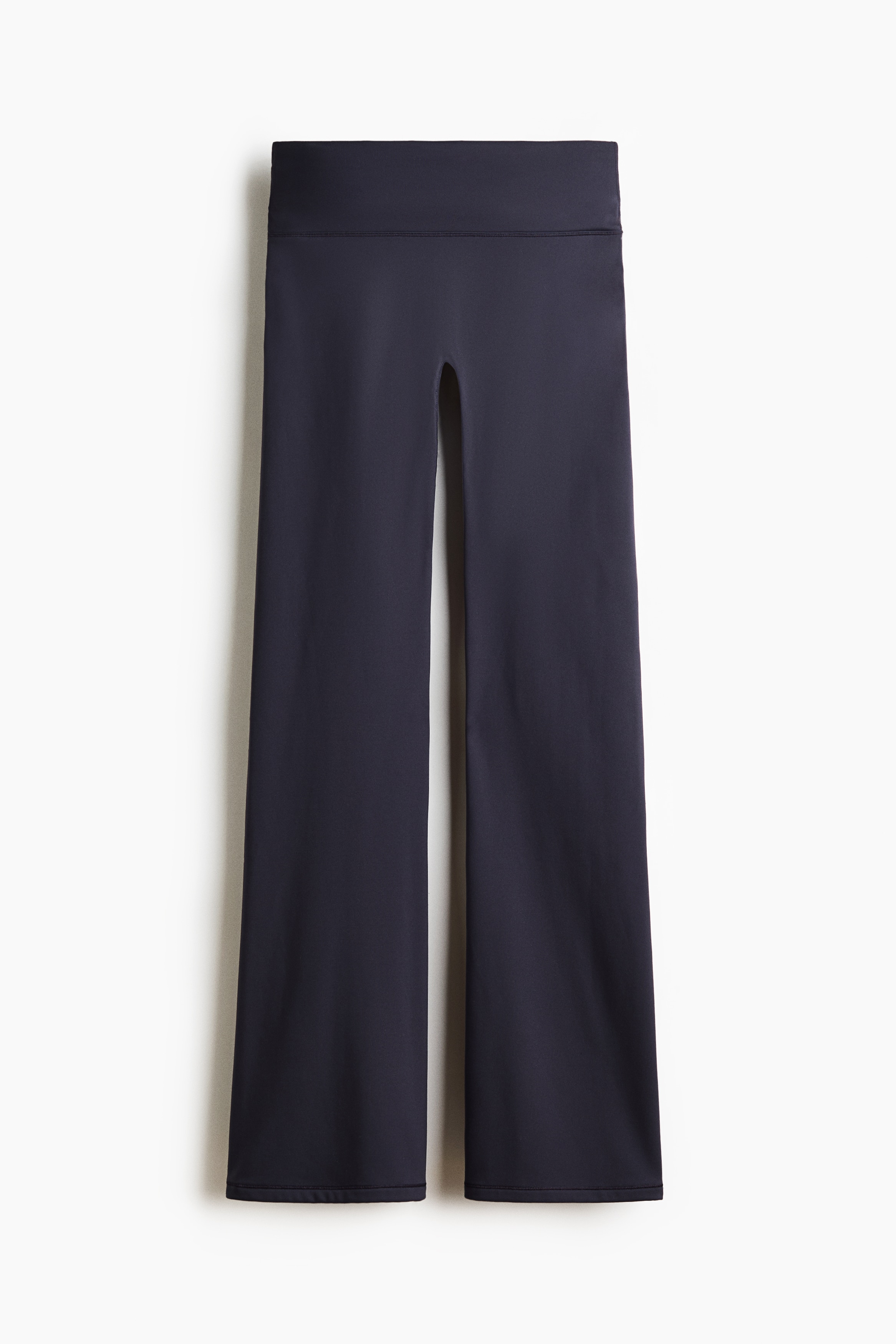 Un ensemble sportif bleu marine foncÃ©, composÃ© dâun haut Ã  manches longues et dâun pantalon Ã©vasÃ© assorti, est portÃ© par le mannequin. Le haut ajustÃ© prÃ©sente des ouvertures pour les pouces aux poignets, tandis que le pantalon taille haute est ajustÃ© sur la jambe et sâÃ©vase lÃ©gÃ¨rement Ã  lâourlet.