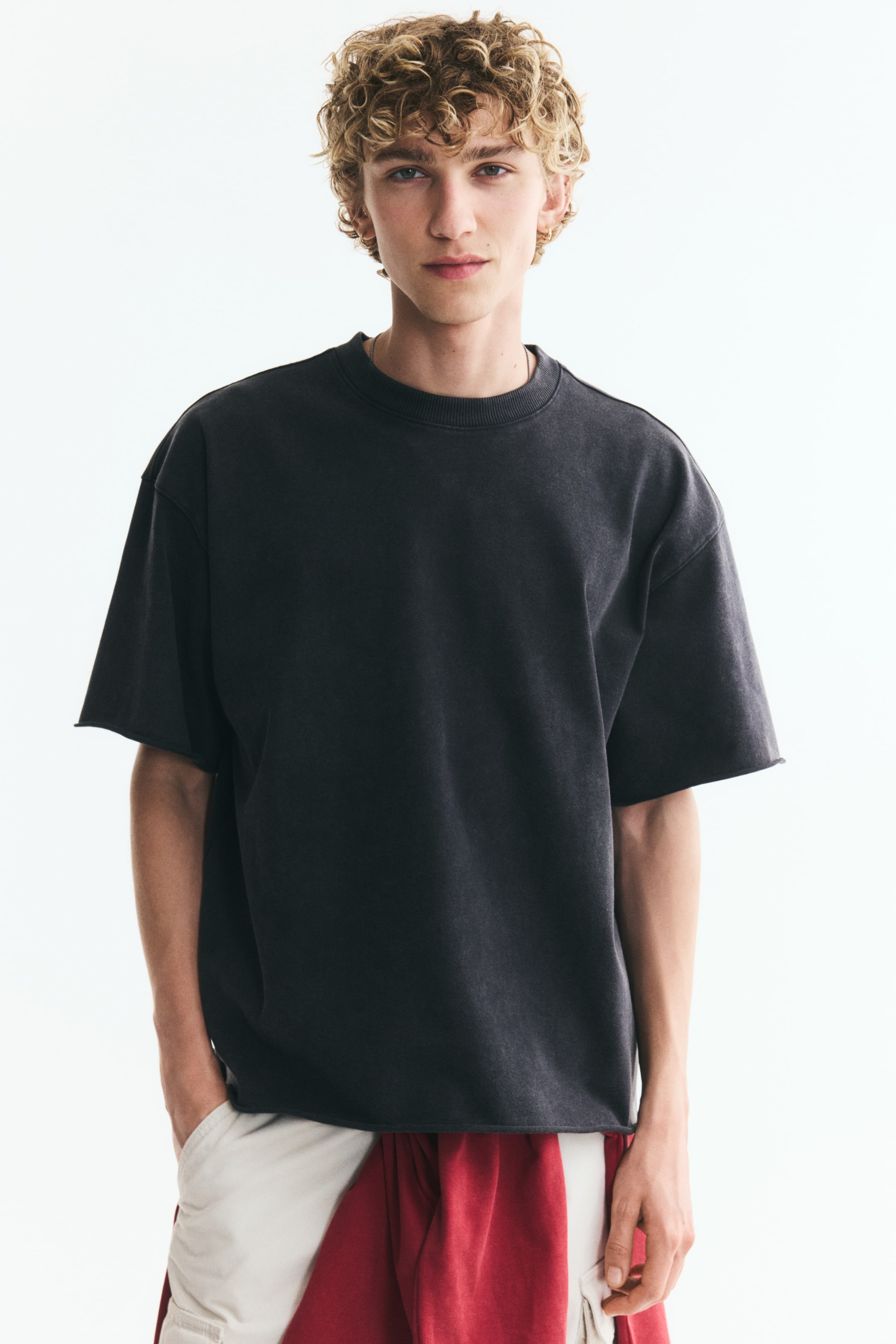Xem ảnh lớn hơn: Người mẫu đang mặc một chiếc áo thun kiểu boxy màu đen washed. Áo có cổ tròn viền bo, vai rớt, và dáng oversized rộng thùng thình với lai áo cắt thẳng.