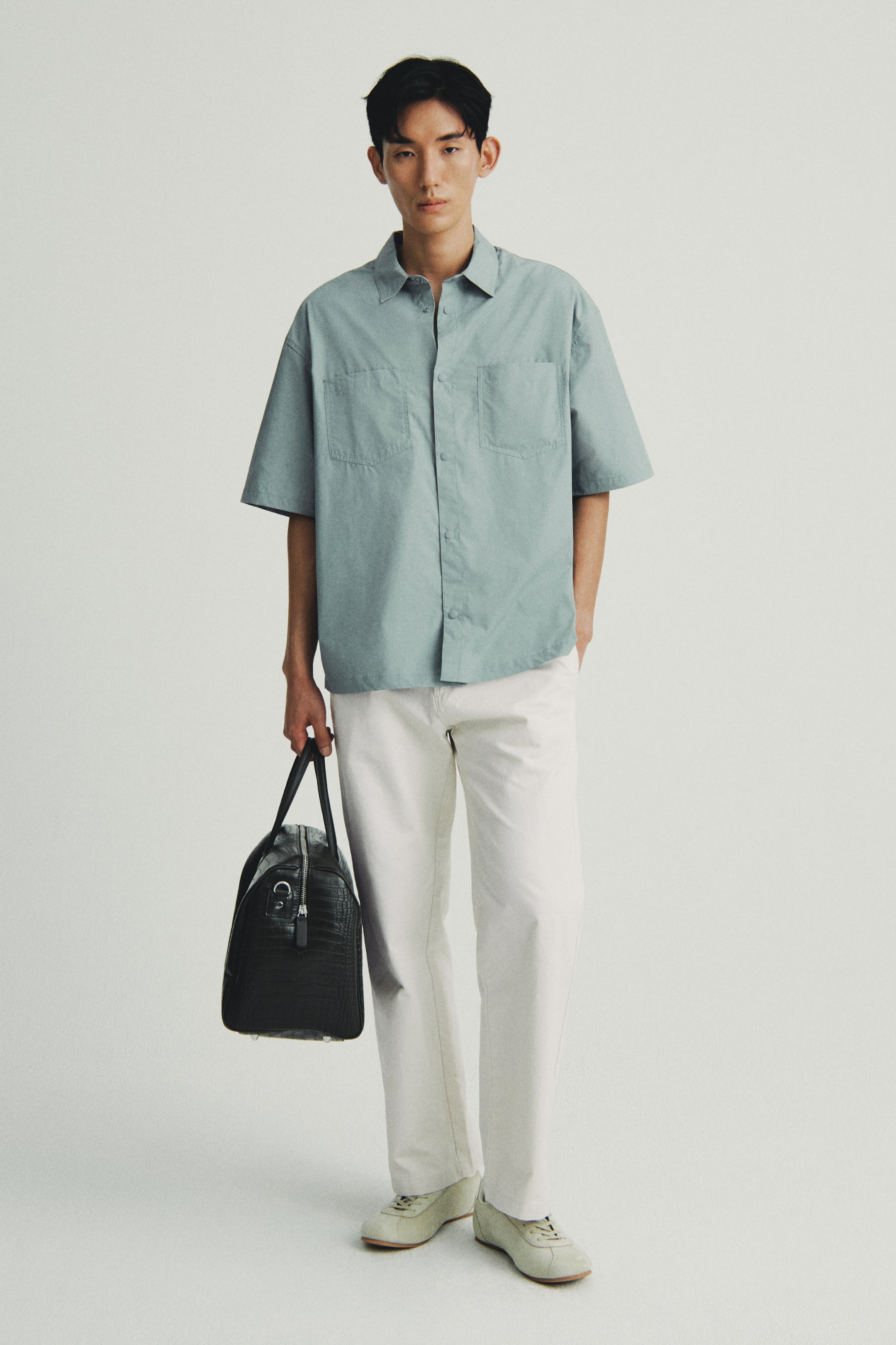 View larger image: A light blue short-sleeved shirt is being presented front-facing, featuring a spread collar and a button-front closure. It is designed with a relaxed fit and includes two flap patch pockets on the chest.
