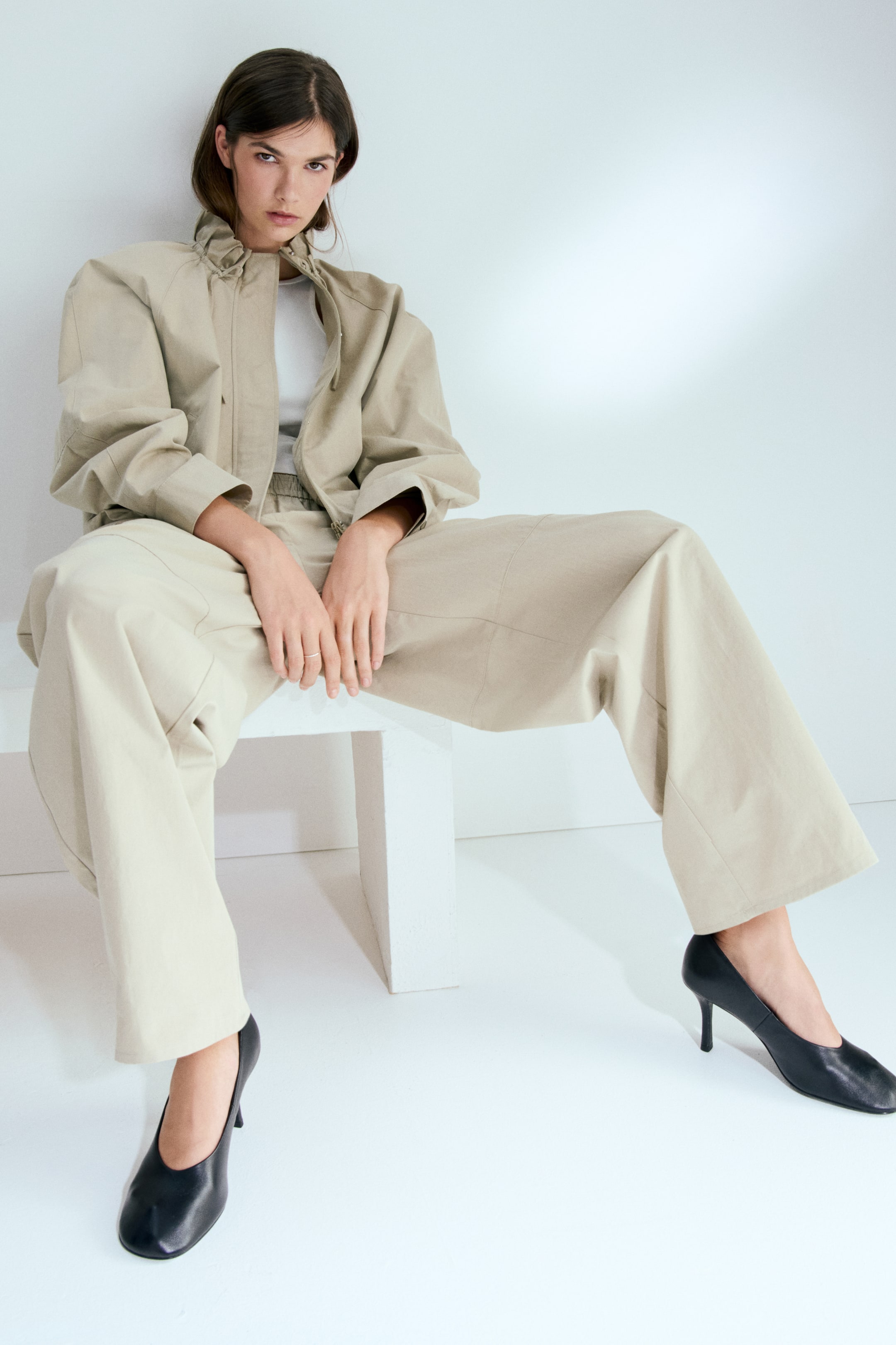 View larger image: Trousers in cotton twill with an elasticated waist and barrel legs are worn by the model. The model is seated, and the trousers drape loosely.