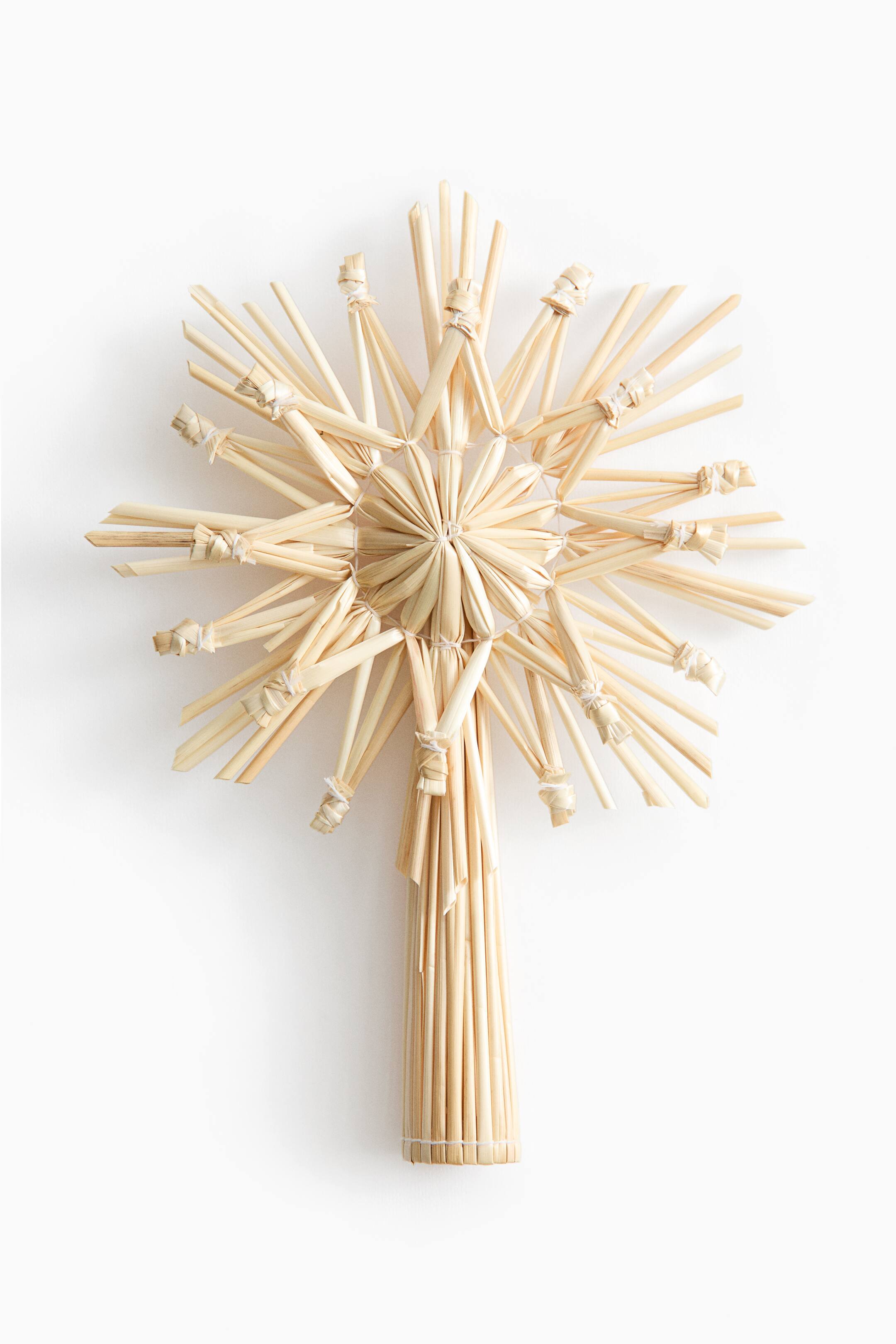 View larger image: A natural straw star tree topper faces forward, showcasing a multi-pointed starburst design made of tied straw stalks. The star extends from a hollow cylindrical base constructed from bundled vertical straws.