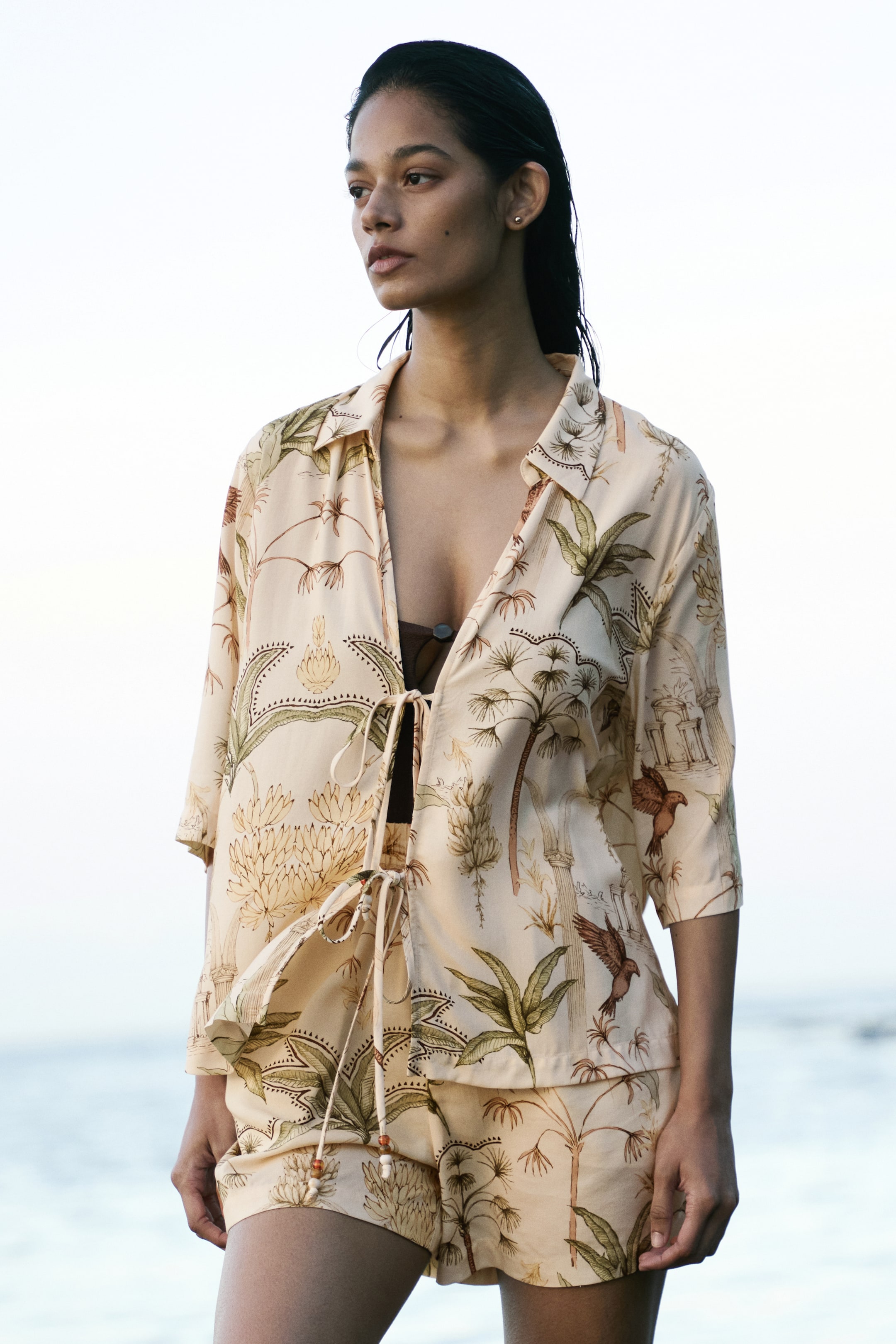 View larger image: The model is showcasing loose-fit shorts crafted from a cream viscose weave adorned with a tropical print. These shorts boast a high waist with smocked elastication and a bead-ended drawstring.