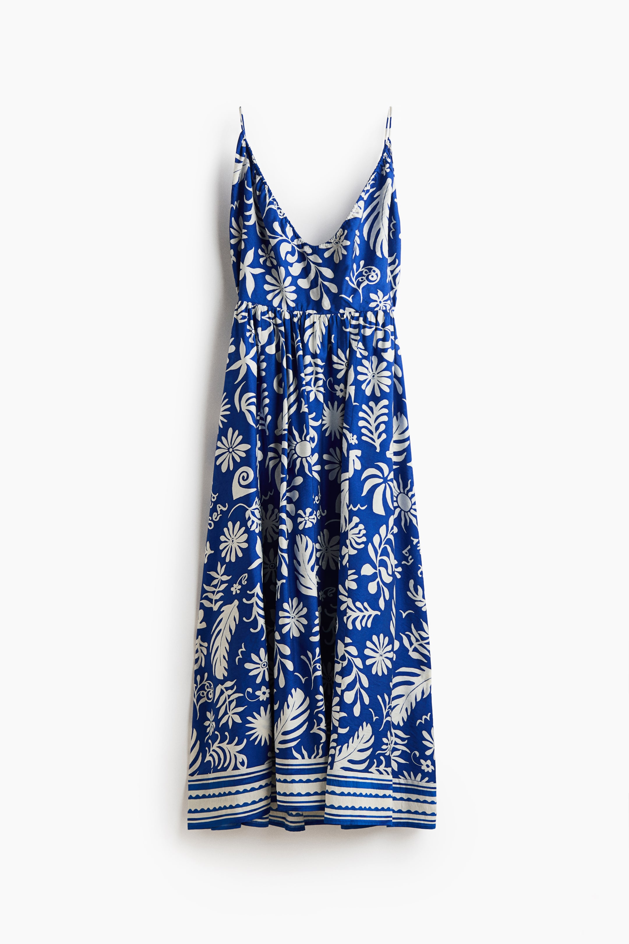 Ampliar la imagen: Un vestido azul de longitud midi tipo slip presenta un patrón floral y botánico blanco en toda la prenda, con tirantes finos tipo espagueti y un escote en V. El vestido destaca por una cintura fruncida y un borde rayado y festoneado blanco en el dobladillo.