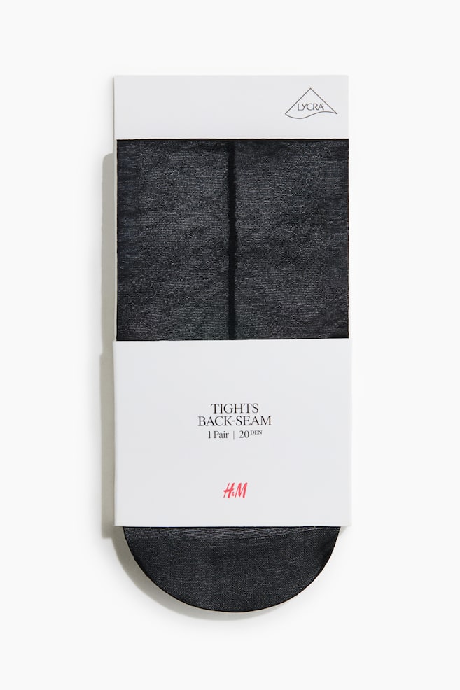 Ein verpacktes Paar transparente schwarze Strumpfhosen ist frontal ausgerichtet und zeigt eine markante vertikale RÃ¼ckennaht, die mittig Ã¼ber den gefalteten Stoff verlÃ¤uft. Das Produkt ist mit einem weissen Papierband umwickelt, auf dem der Text Â«TIGHTS BACK-SEAM \| 1 Pair \| 20 DENÂ» sowie ein rotes H&M-Logo zu sehen sind. - 1