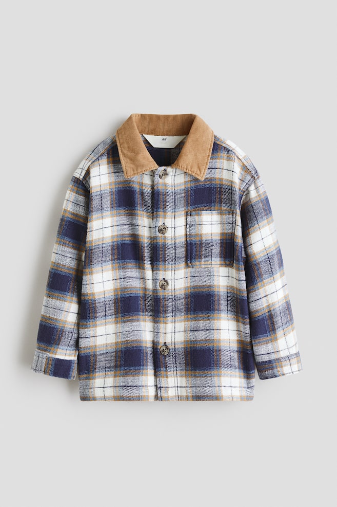 A checked shirt jacket is presented front-facing, featuring a white, navy blue, and camel check pattern. It is designed with a contrasting light brown corduroy collar, a button-up front with dark buttons, and a single patch pocket appearing on the left chest. - 1