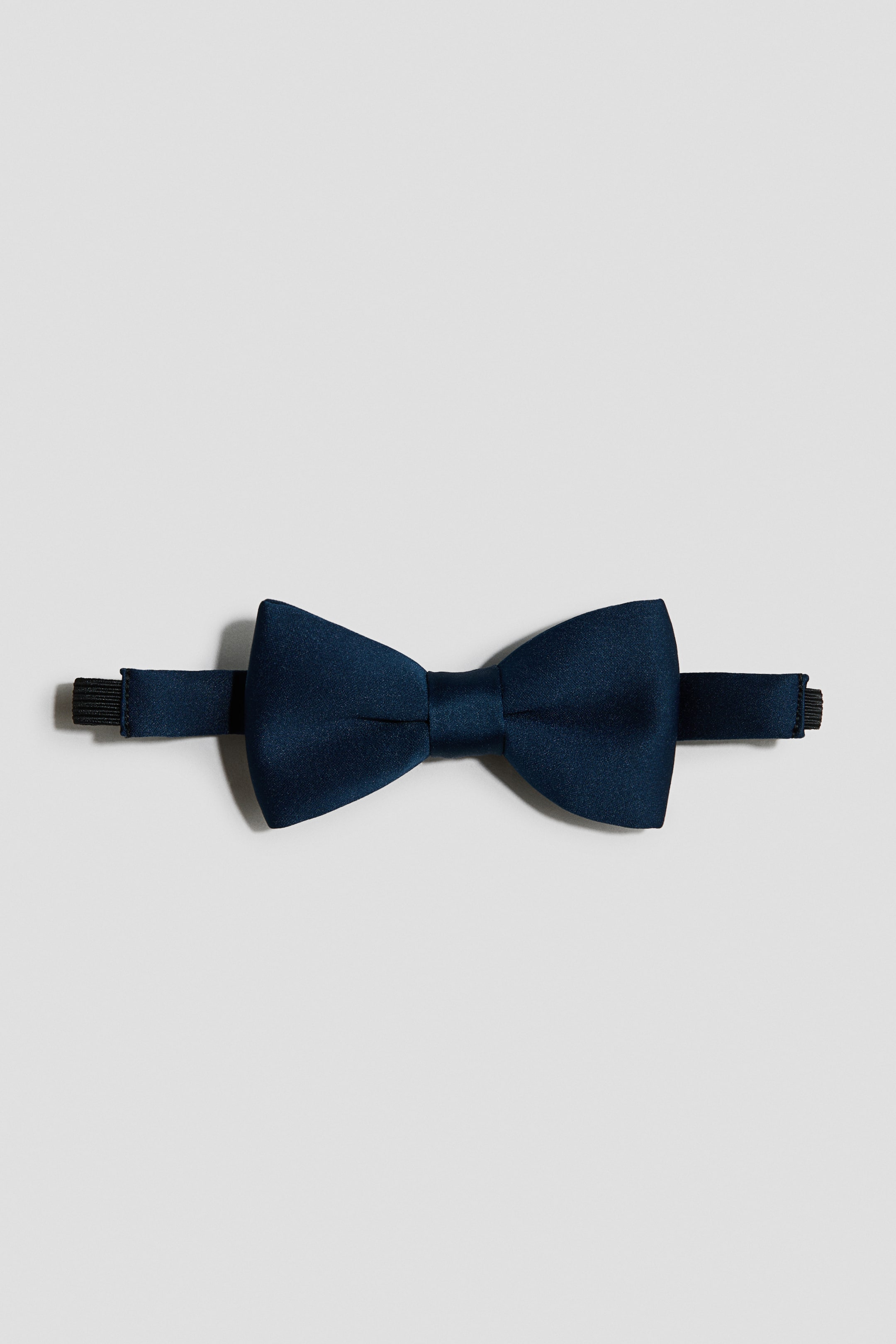 View larger image: A navy blue bow tie featuring a classic bow shape with a subtle sheen, connected to a black adjustable neck strap.