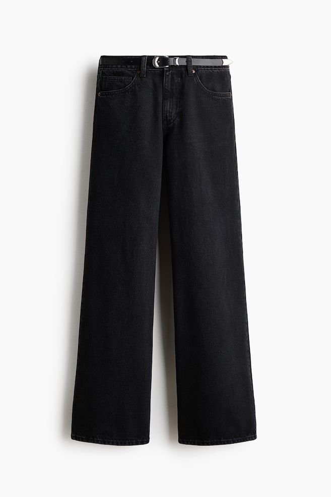 Ett par svarta vida jeans visas framifrÃ¥n och har en klassisk femficksdesign samt en avslappnad, rak silhuett. Jeansen Ã¤r stylade med ett smalt svart bÃ¤lte trÃ¤dd genom hÃ¤llorna i midjan, med ett polerat spÃ¤nne, hÃ¥llare och metalldel i silverton. - 1