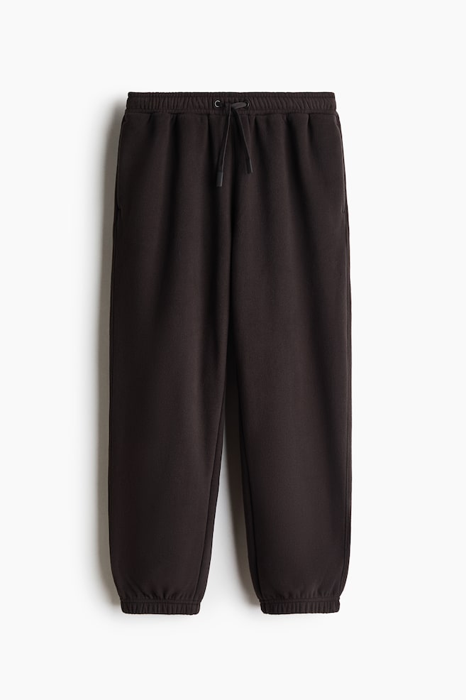 Dunkelbraune Fleece-Sweatpants sind von vorne zu sehen und zeichnen sich durch ein locker geschnittenes Design mit elastischem Bund, passendem verstellbarem Kordelzug und elastischen BÃ¼ndchen an den SaumabschlÃ¼ssen aus. - 1