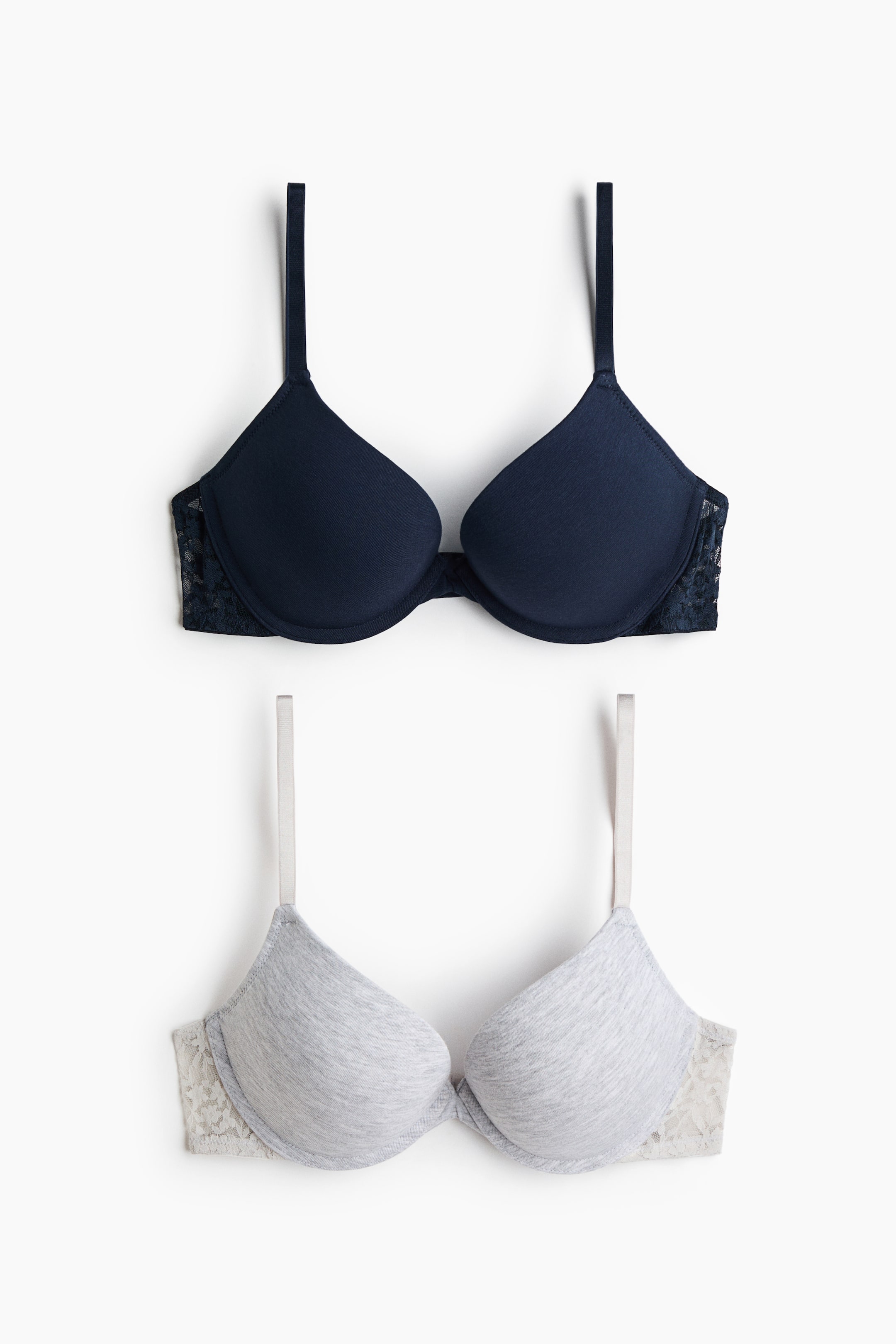 View larger image: Two push-up bras are shown from the front, featuring moulded, padded cups in soft cotton jersey with delicate lace side panels. The top bra is dark navy blue with matching lace, and the bottom bra is light heather grey with contrasting cream-coloured lace.