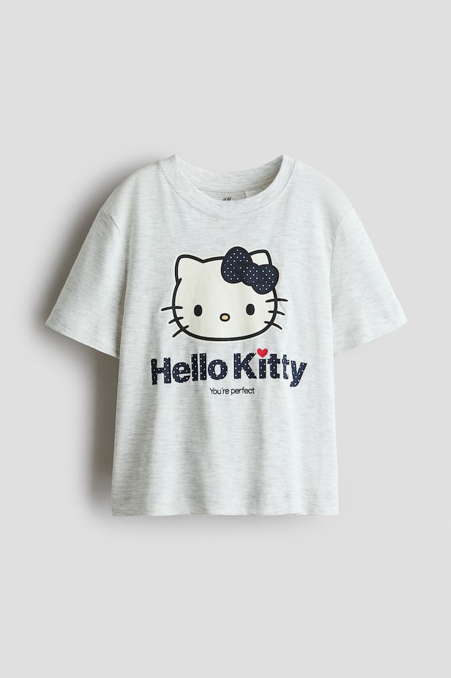 A light grey jersey tee is shown from the front, featuring a round rib-trimmed neckline and short sleeves. The shirt displays a printed graphic of Hello Kitty wearing a dark blue polka-dot bow, placed above the printed text âHello Kittyâ and âYouâre perfectâ. - 1