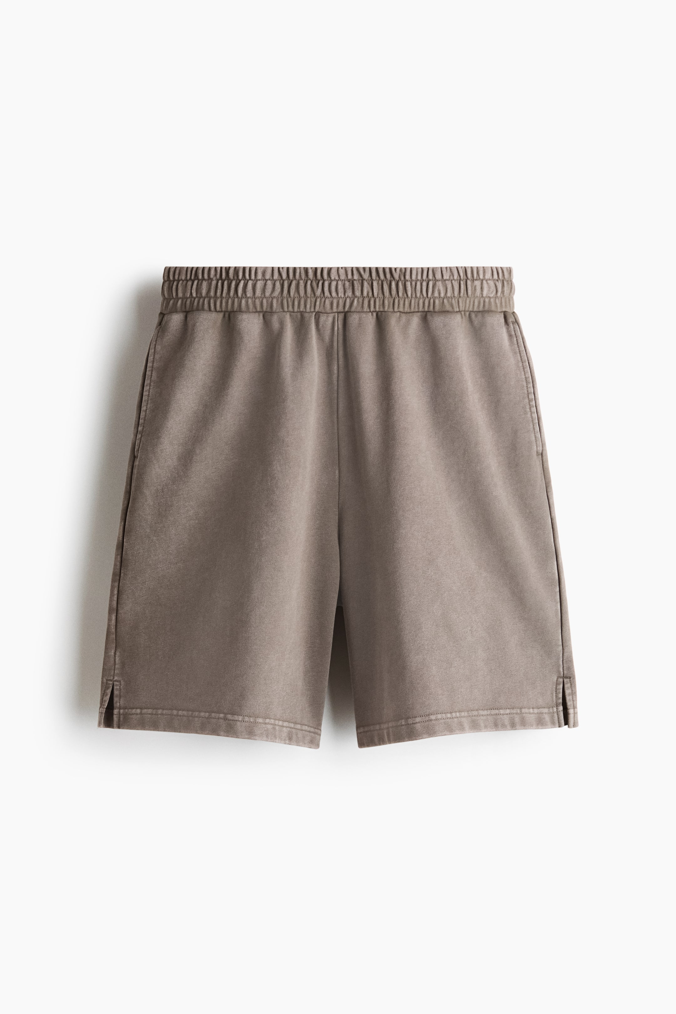 View larger image: A pair of faded taupe shorts featuring an elasticised waistband and side pockets. Small slits are visible at the bottom hem.
