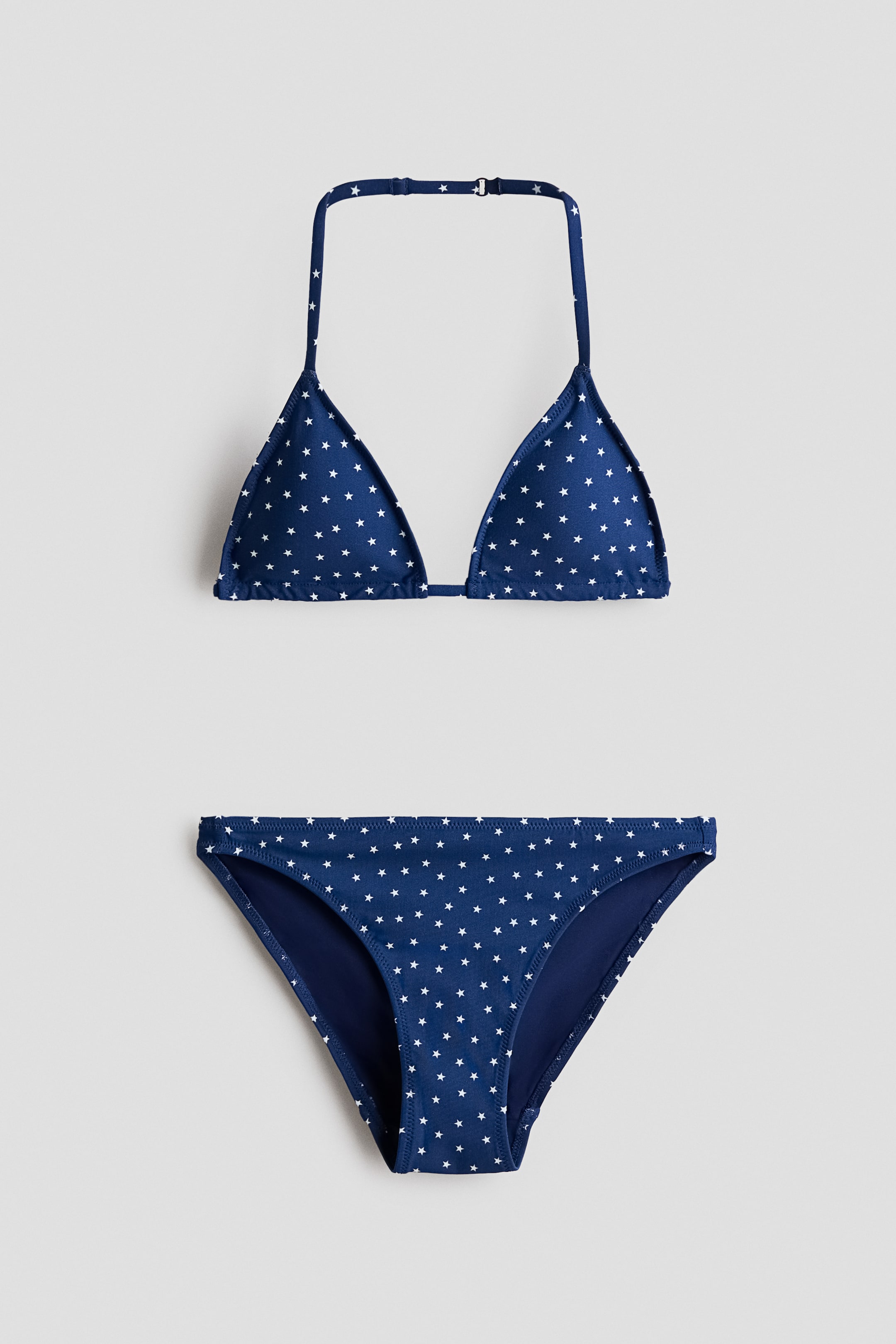 Grösseres Bild ansehen: Ein dunkelblaues Bikini-Set mit einem weißen Sternenmuster wird von vorne präsentiert. Das Triangel-Bikini-Oberteil zeigt einen verstellbaren Neckholder-Träger, und die dazu passenden Bikini-Hosen vervollständigen das Set.