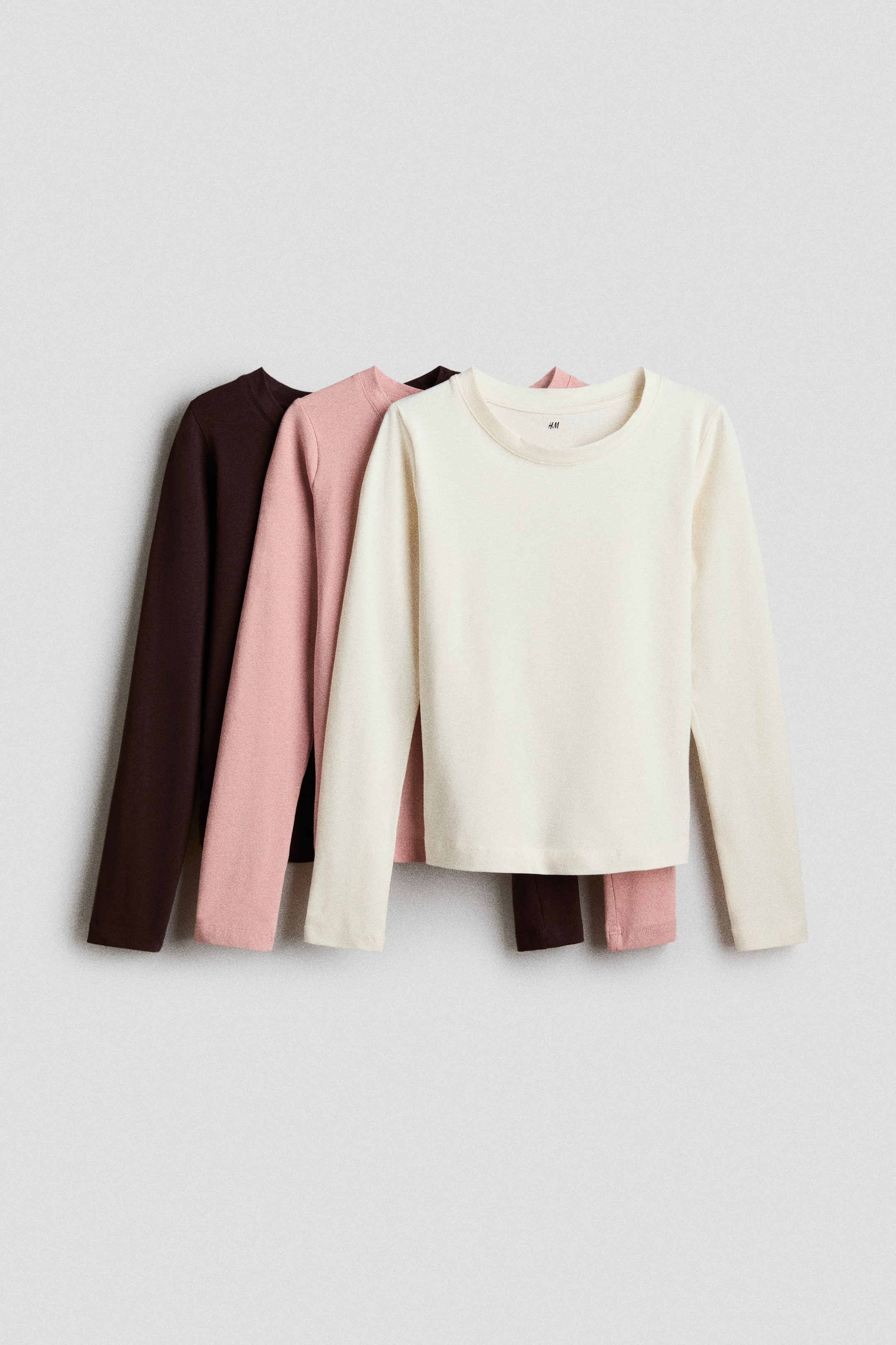 Se større billede: Tre langærmede T-shirts i blød bomuldsjersey er lagdelt, hvor den forreste T-shirt er råhvid. T-shirtsene har rund hals med smalle ribkanter og lange ærmer, mens de øvrige to T-shirts fremstår i pink og brun.