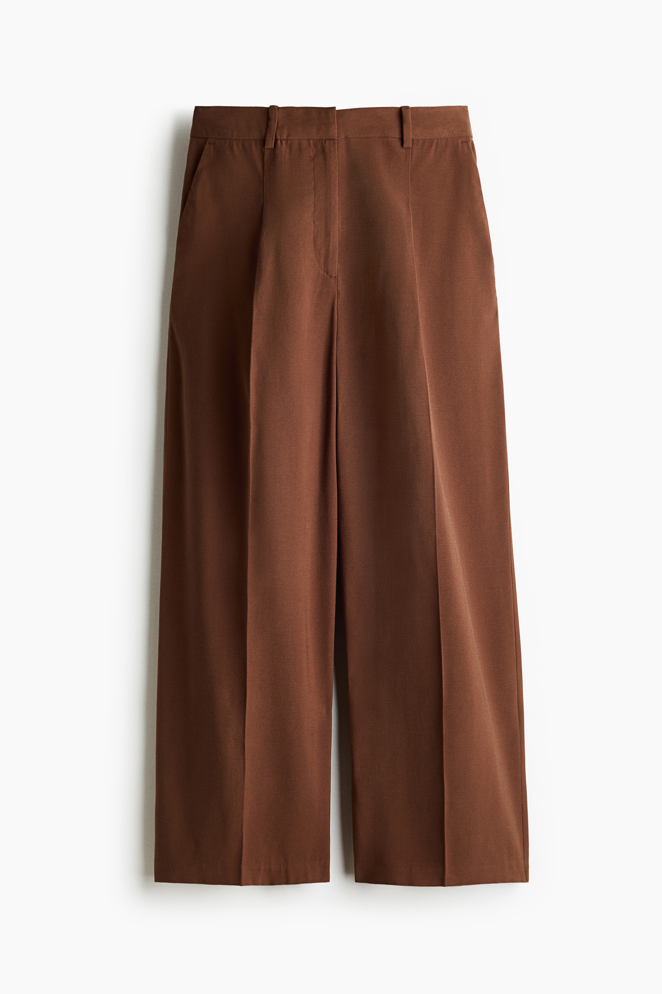 View larger image: A pair of brown wide-leg trousers is shown from the front, featuring a high-waisted fit with belt loops and a concealed front fastening. The trousers feature front pleats, sharp creases running down the centre of each leg, and side slip pockets.