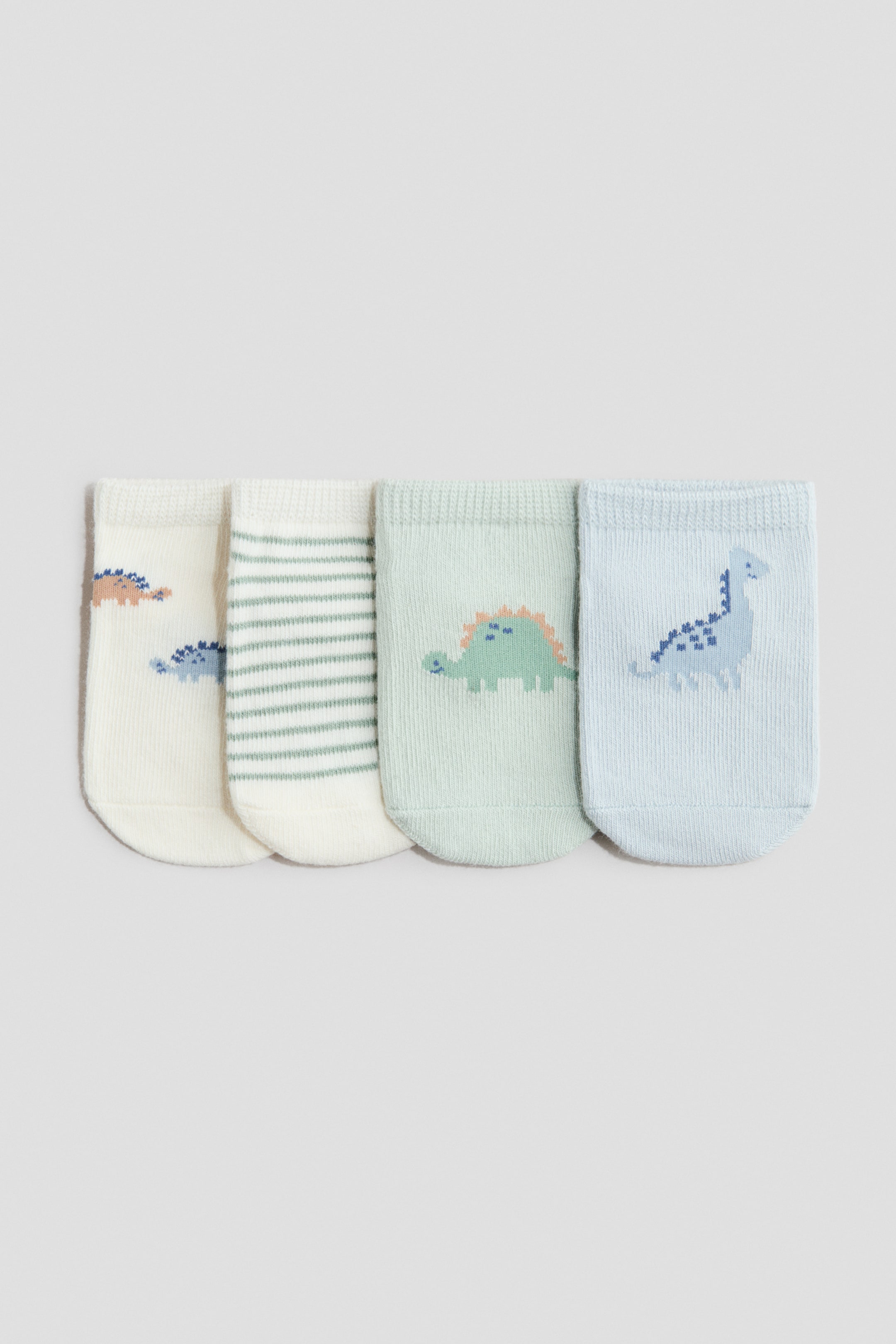 View larger image: Four shaftless socks are lying flat, showcasing their front view. Crafted from a soft, fine-knit cotton blend, these socks feature elasticated tops for a comfortable fit. Two of the socks come in a cream hue, with one displaying designs of blue and muted orange dinosaurs, while the other boasts green horizontal stripes. The remaining two socks include a light mint green one, adorned with a green dinosaur featuring muted orange spikes, and a light blue one, which highlights a blue dinosaur with darker blue spots.
